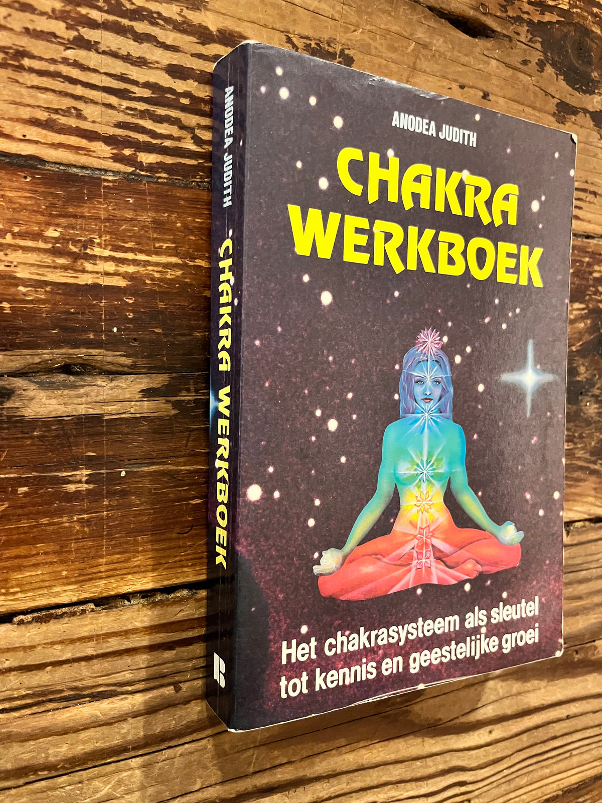 Voorkant en rug van boek met de titel 'Chakra werkboek' door Andrea Judith op een houten achtergrond 