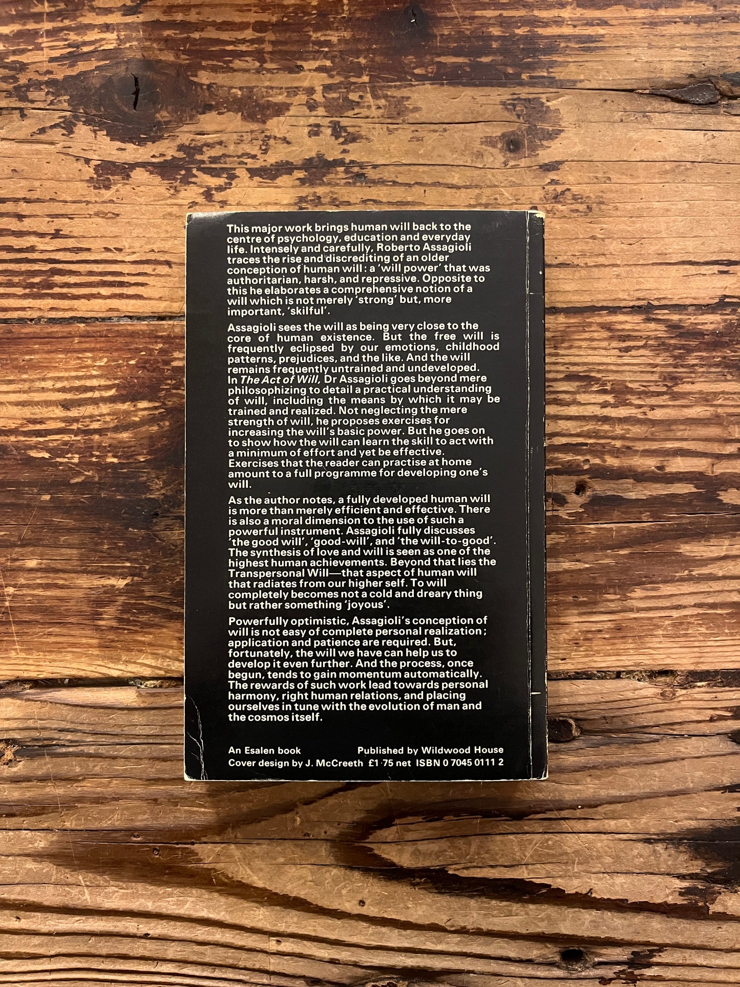 Back cover of book titled 'The Act of Will' by Roberto Assagioli on a wooden surface