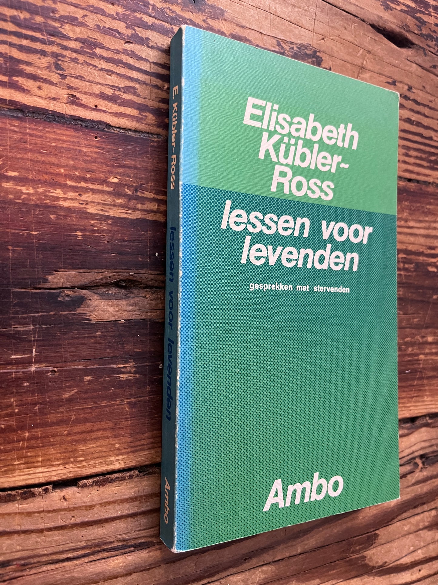Rug en voorkant van boek met de titel 'lessen voor levenden' door Elisabeth Kübler-Ross   op een houten achtergrond 