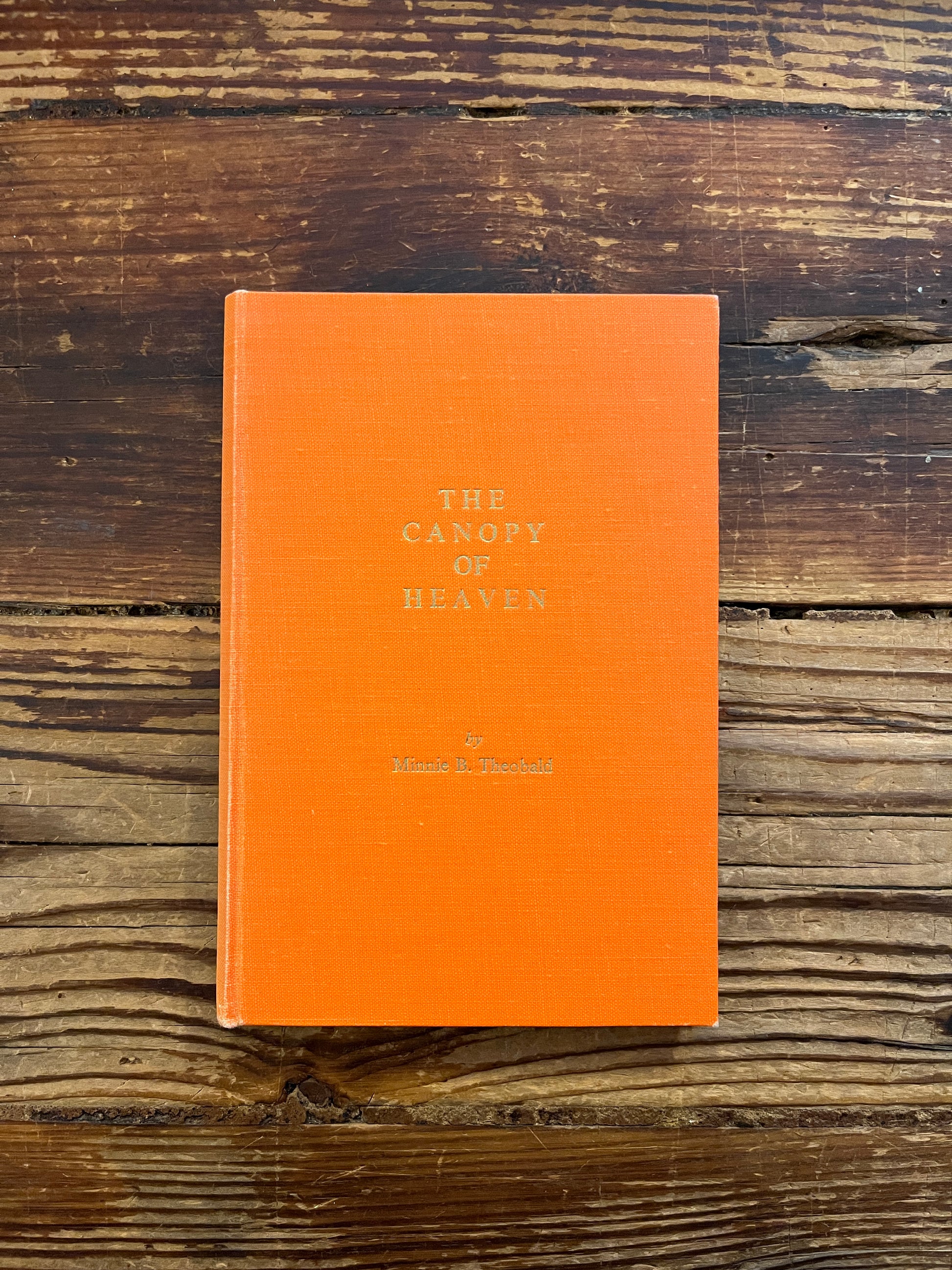 Front cover of book titled 'the canopy of heaven' by Minnie Theobald on a wooden surface
