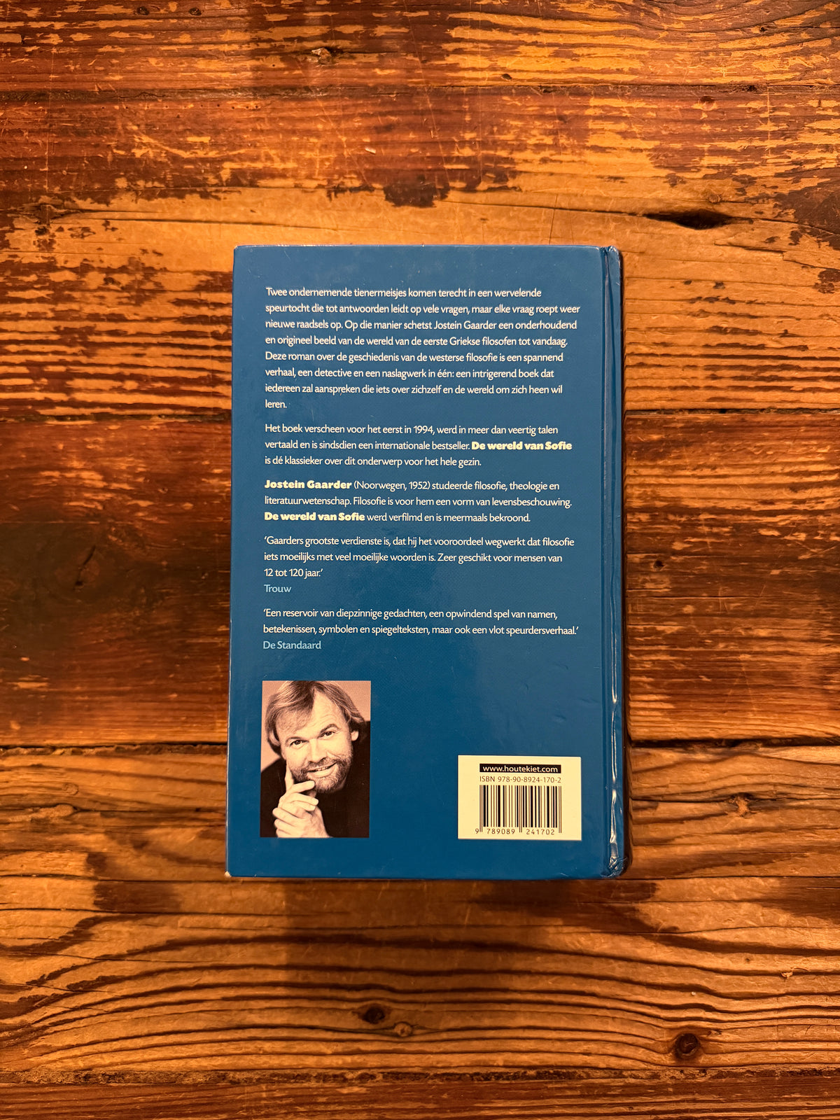 Achterkant van boek met de titel 'De wereld van Sofie' door Jostein Gaarder, op een houten achtergrond