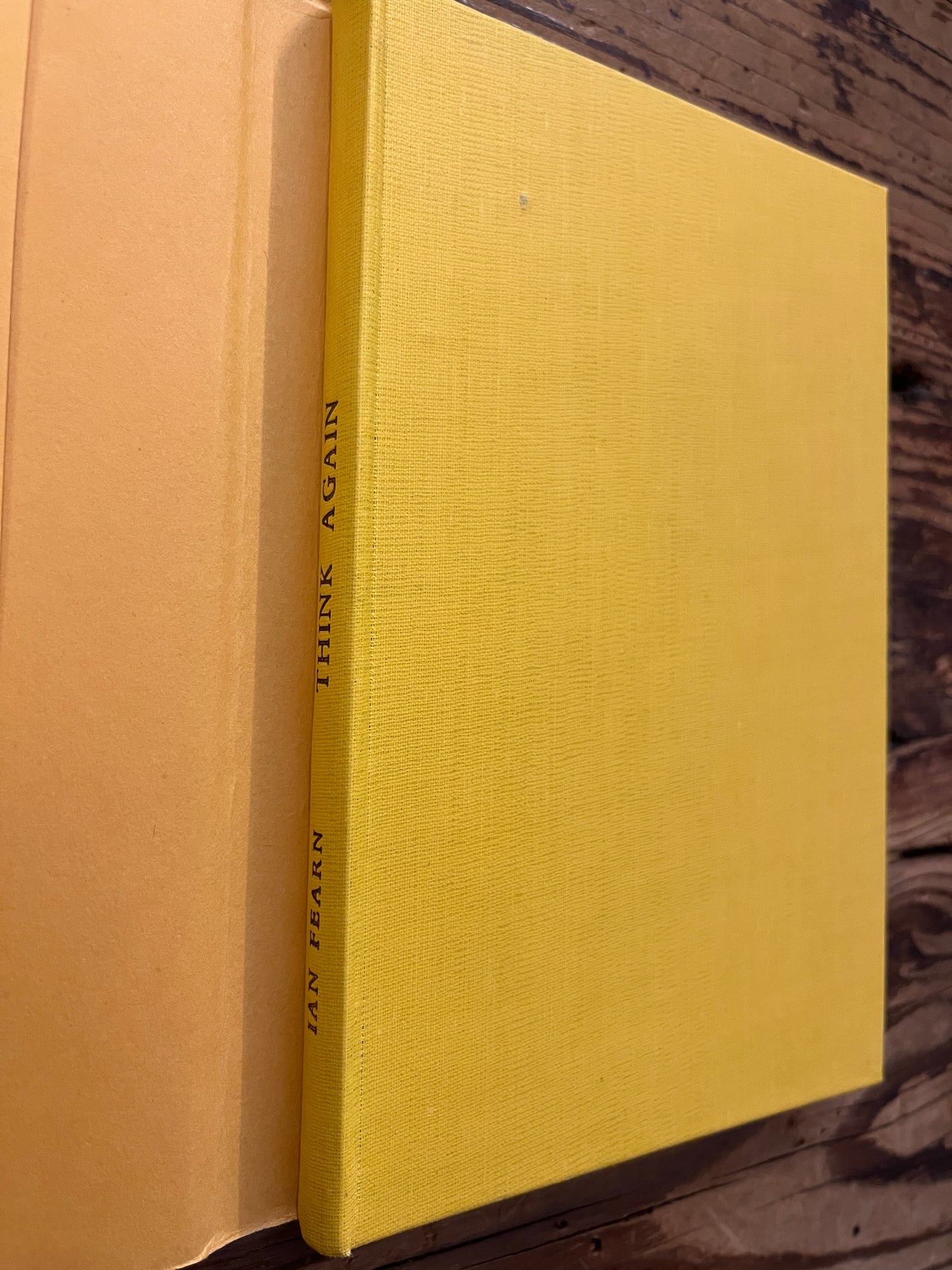 Yellow cloth book without dust jacket with the title 'Think Again' by Ian Fearn on a wooden surface