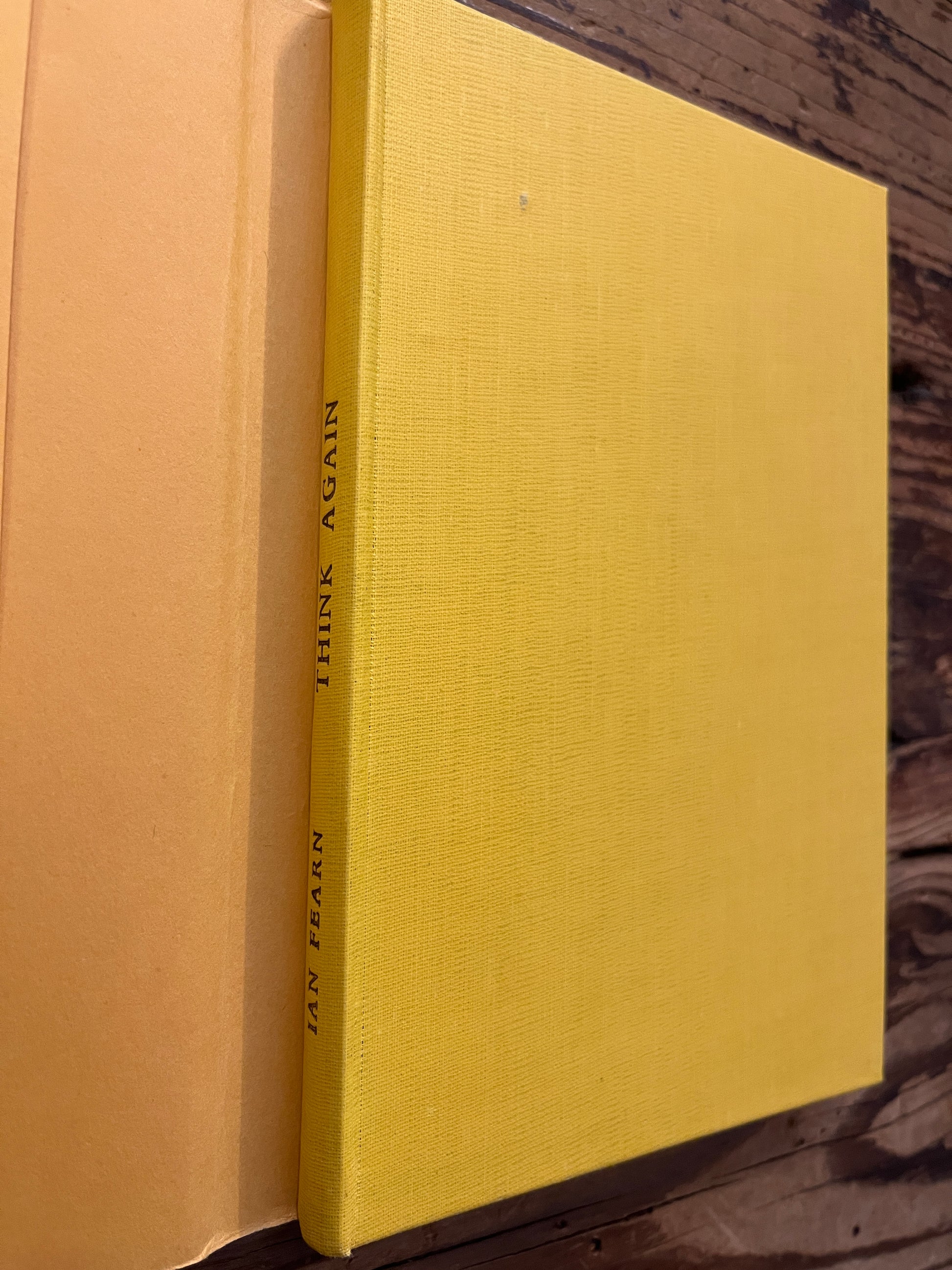 Yellow cloth book without dust jacket with the title 'Think Again' by Ian Fearn on a wooden surface