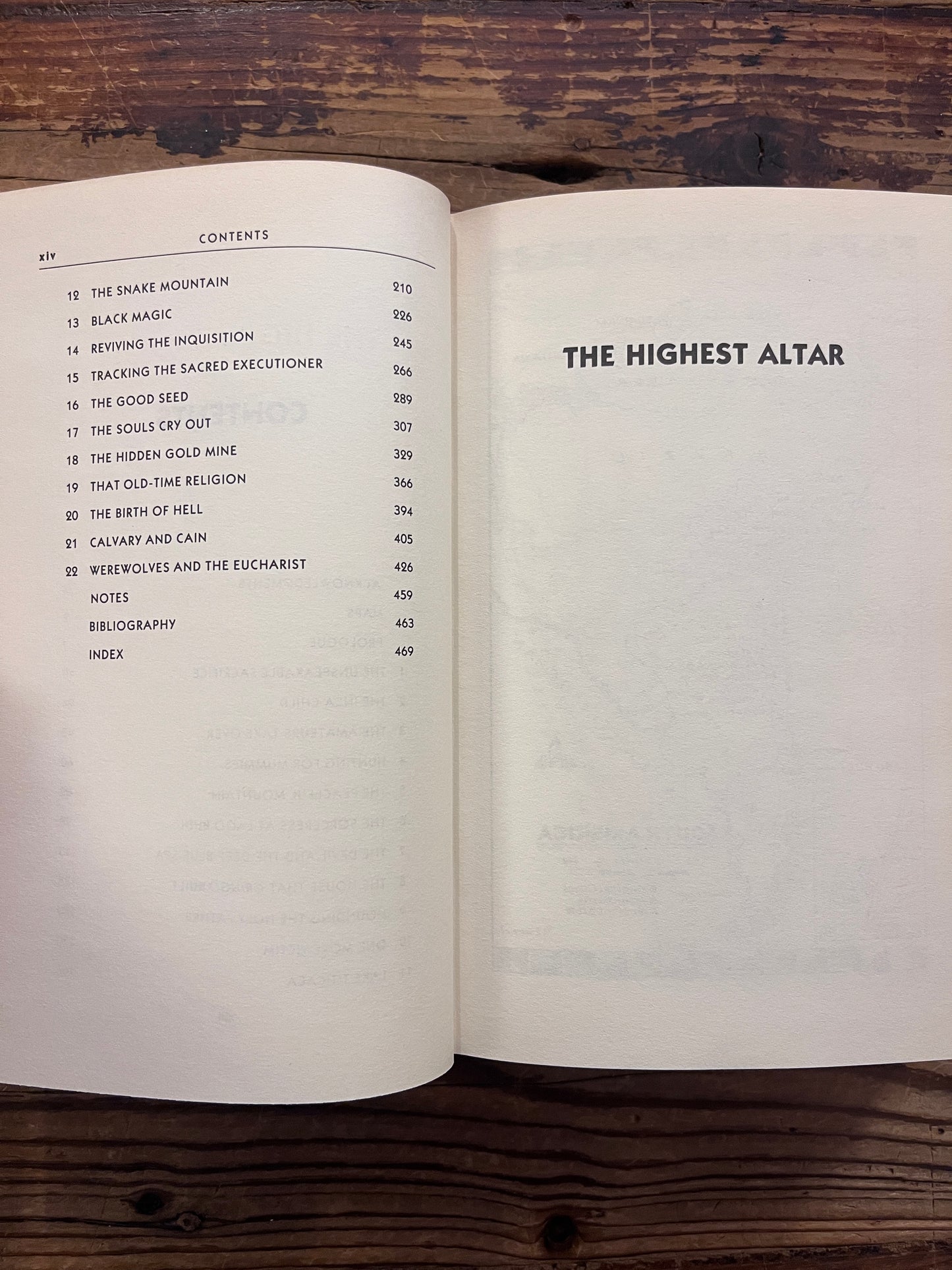 Open book with the title 'The Highest Altar: The Story of Human Sacrifice' by Patrick Tierney is displayed on a wooden surface