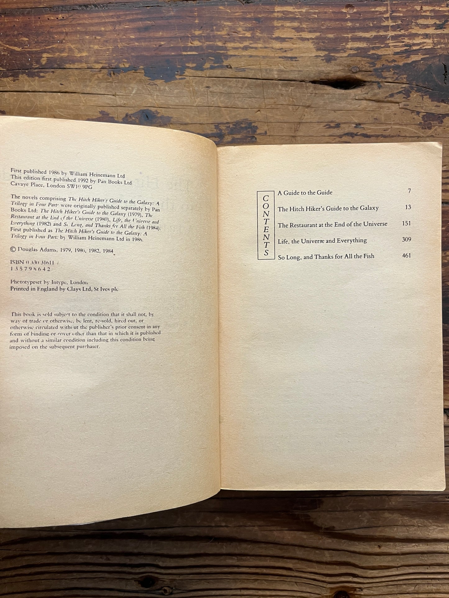 Open book titled 'The Hitchhiker's Guide to the Galaxy' by Douglas Adams on a wooden surface