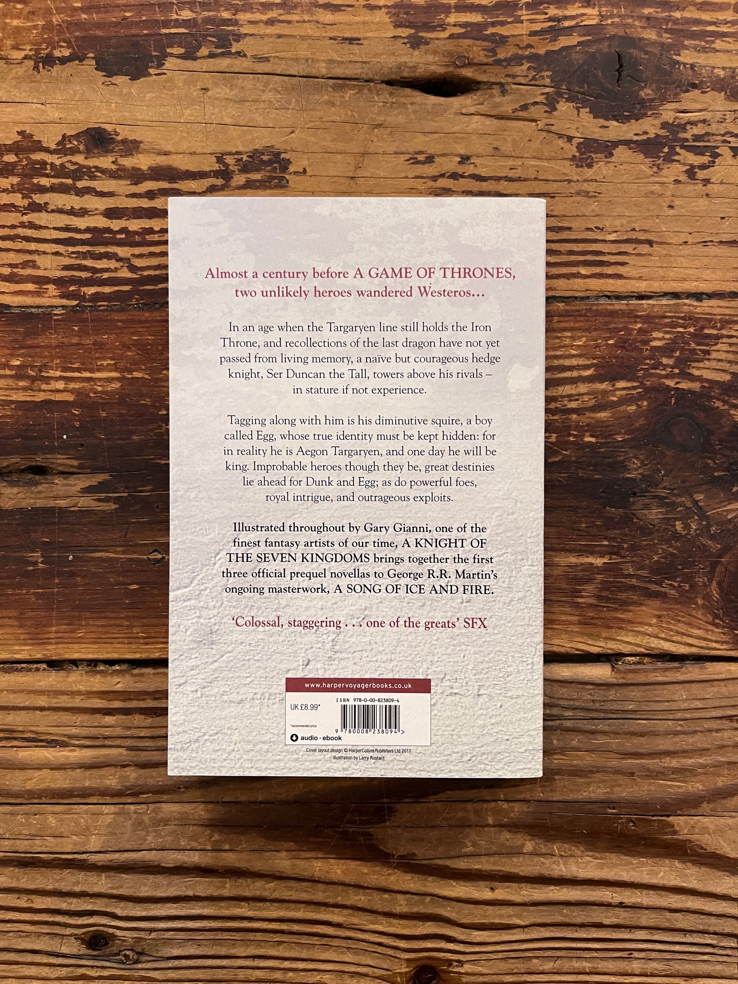 Back cover of book titled 'A Knight of the Seven Kingdoms' by George R.R. Martin on a wooden surface