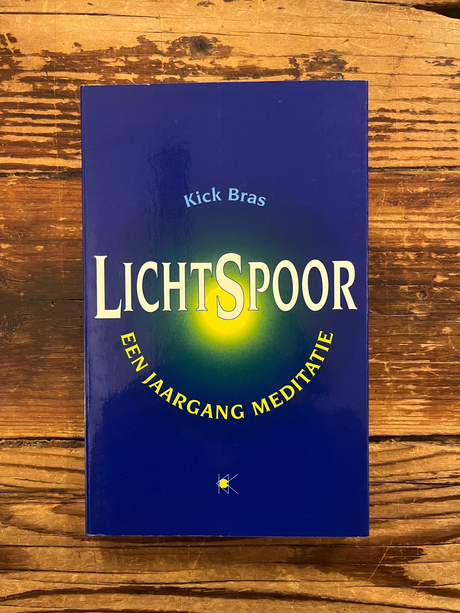 Voorkant van boek 'lichtspoor' door Kick Bras op een houten achtergrond 