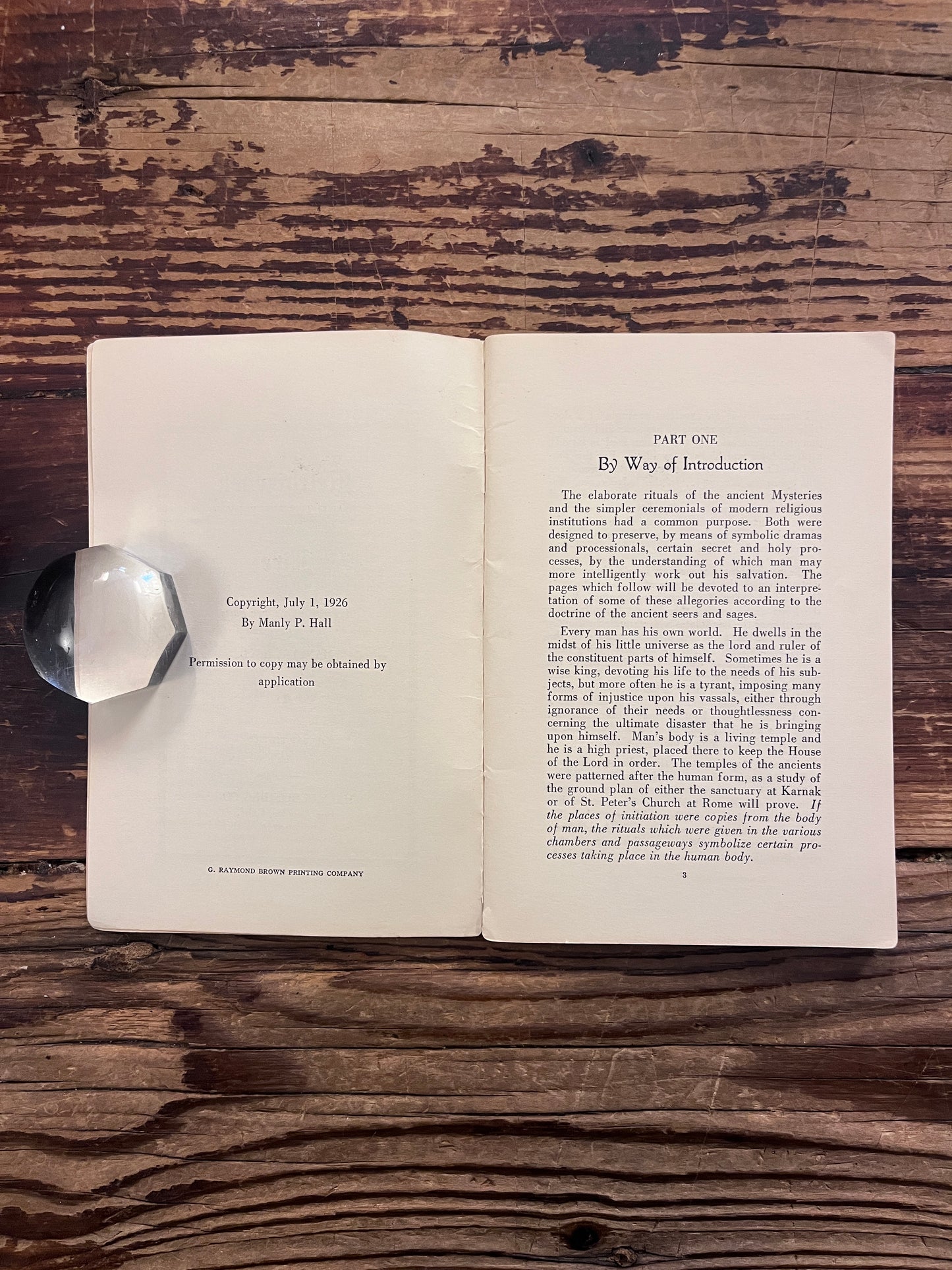 Open booklet titled 'Melchizedek and the mystery of fire' by Manly P. Hall on a wooden surface 