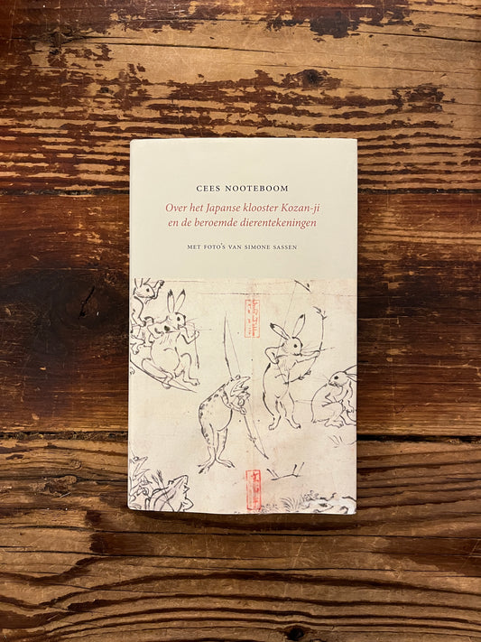 Voorkant van boek met de titel 'Over het Japanse klooster Kozan-ji en de beroemde dierentekeningen' door Cees Nooteboom, op een houten achtergrond