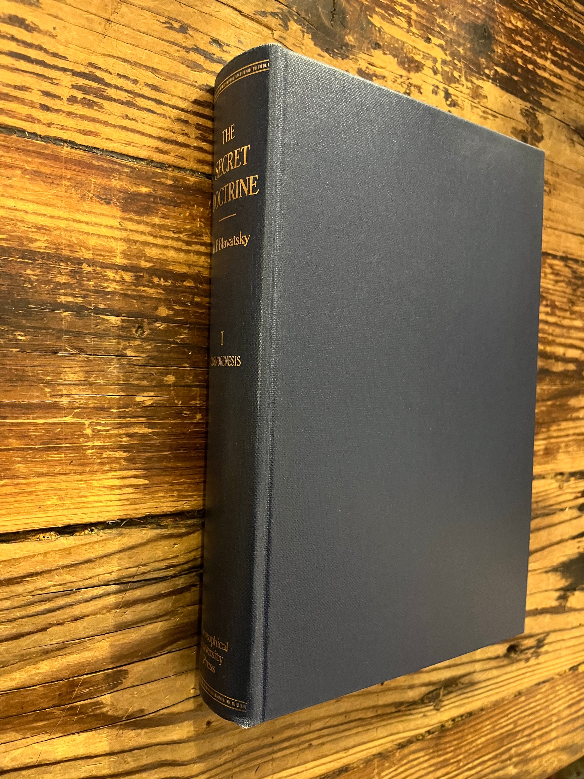 Book without dust jacket titled 'The Secret Doctrine' by H.P. Blavatsky on a wooden surface.