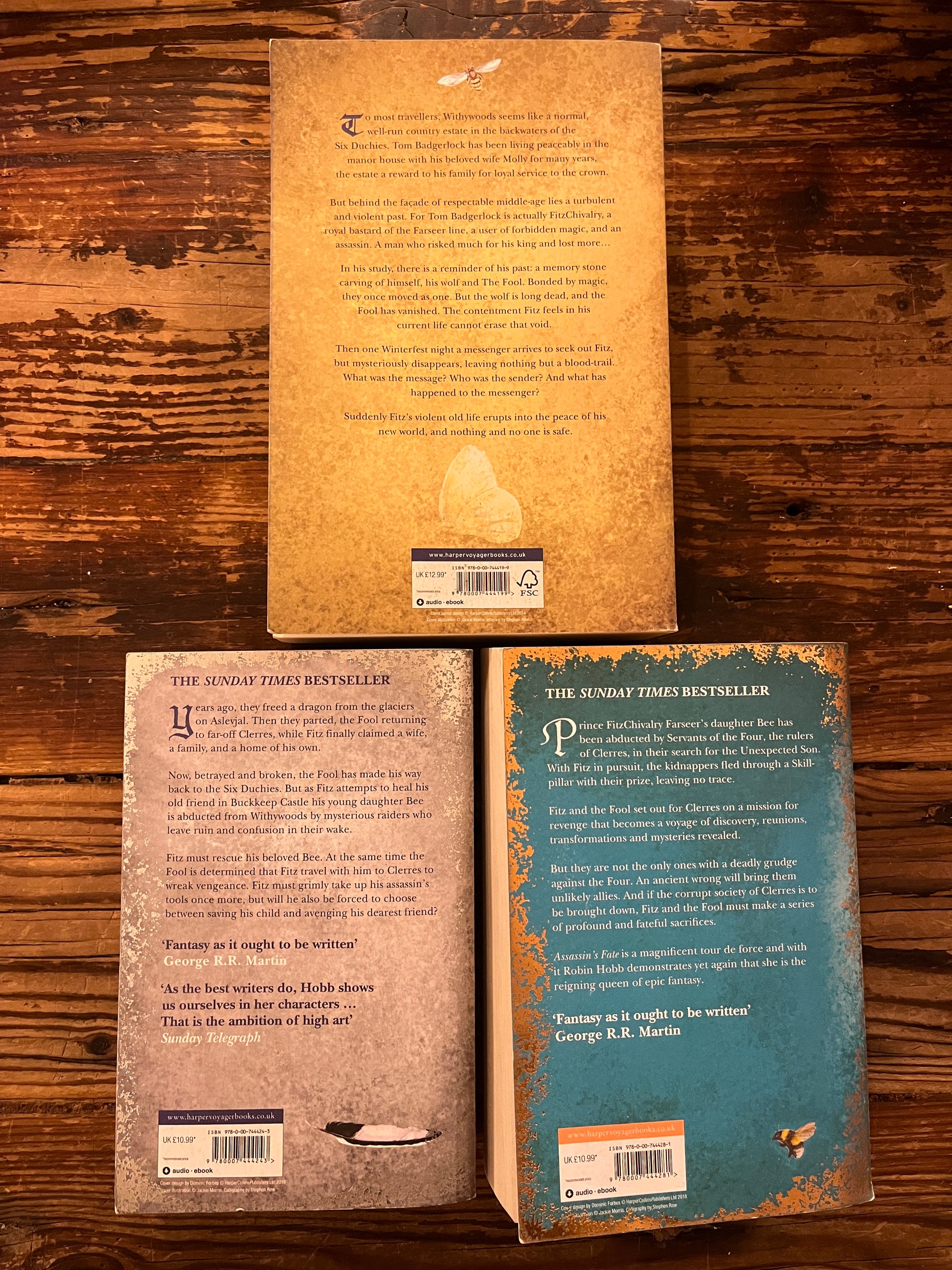 Three books titled 'Assassin's Fate', 'Fool's Quest', and 'Fool's Assassin' by Robin Hobb on a wooden surface.