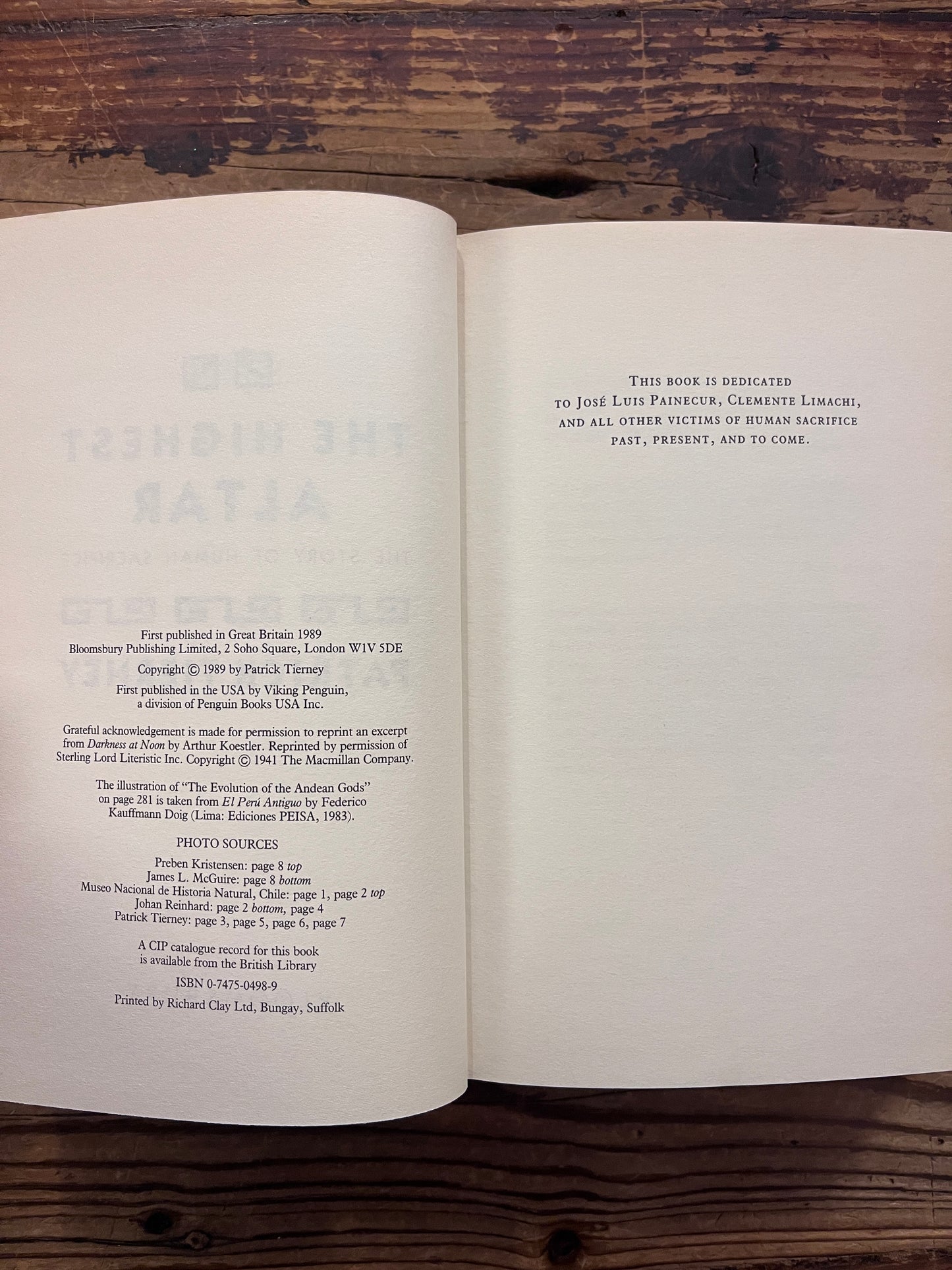 Open book with the title 'The Highest Altar: The Story of Human Sacrifice' by Patrick Tierney is displayed on a wooden surface