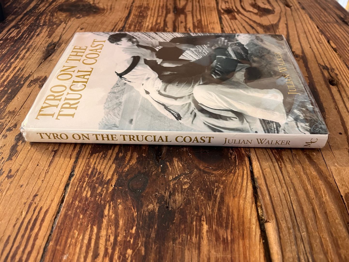 Spine and front cover of book (with dust jacket) with the title 'Tyro on the Trucial Coast' by Julian Walker on a wooden surface