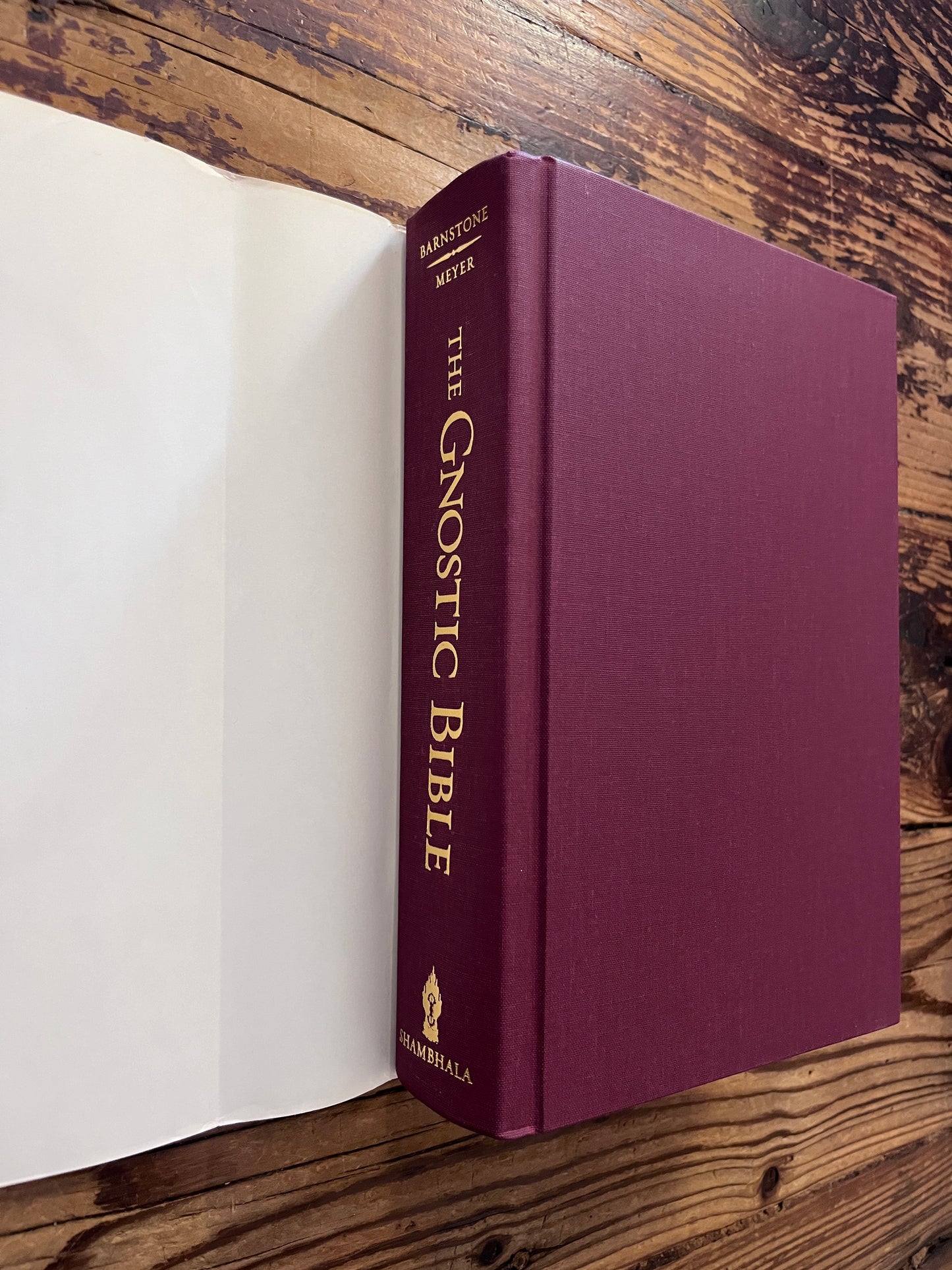 Front cover and spine without dust jacket of book titled 'he Gnostic Bible' edited by Willis Barnstone and Marvin Meyer, on a wooden surface