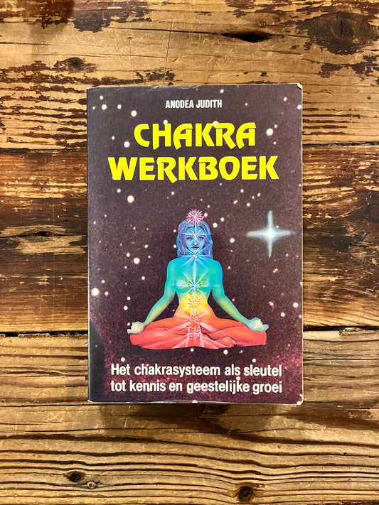 Voorkant van boek met de titel 'Chakra werkboek' door Andrea Judith op een houten achtergrond 