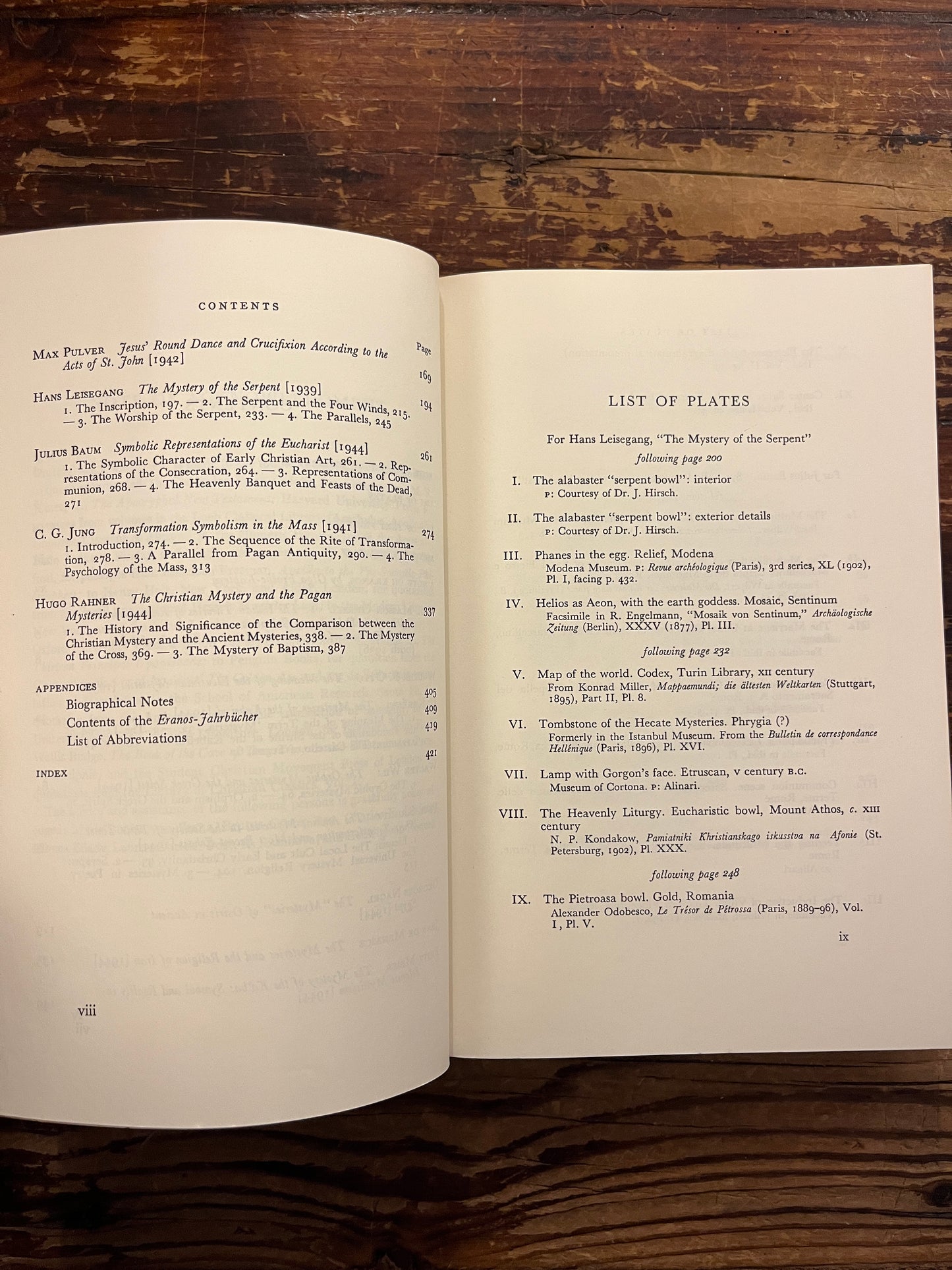 Open book showing the contents of book titled 'The Mysteries, papers from the Eranos Yearbooks' on a wooden surface