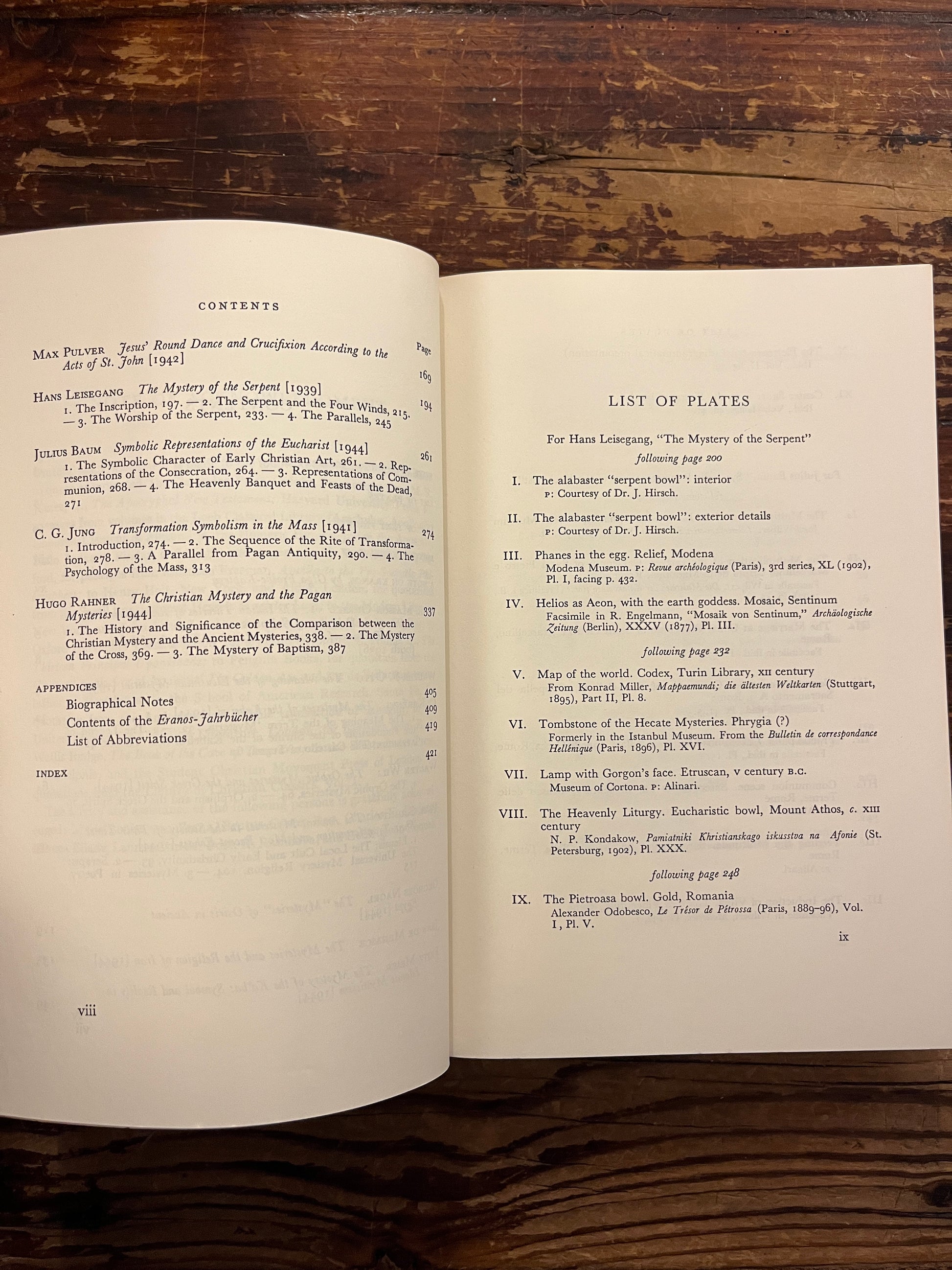 Open book showing the contents of book titled 'The Mysteries, papers from the Eranos Yearbooks' on a wooden surface