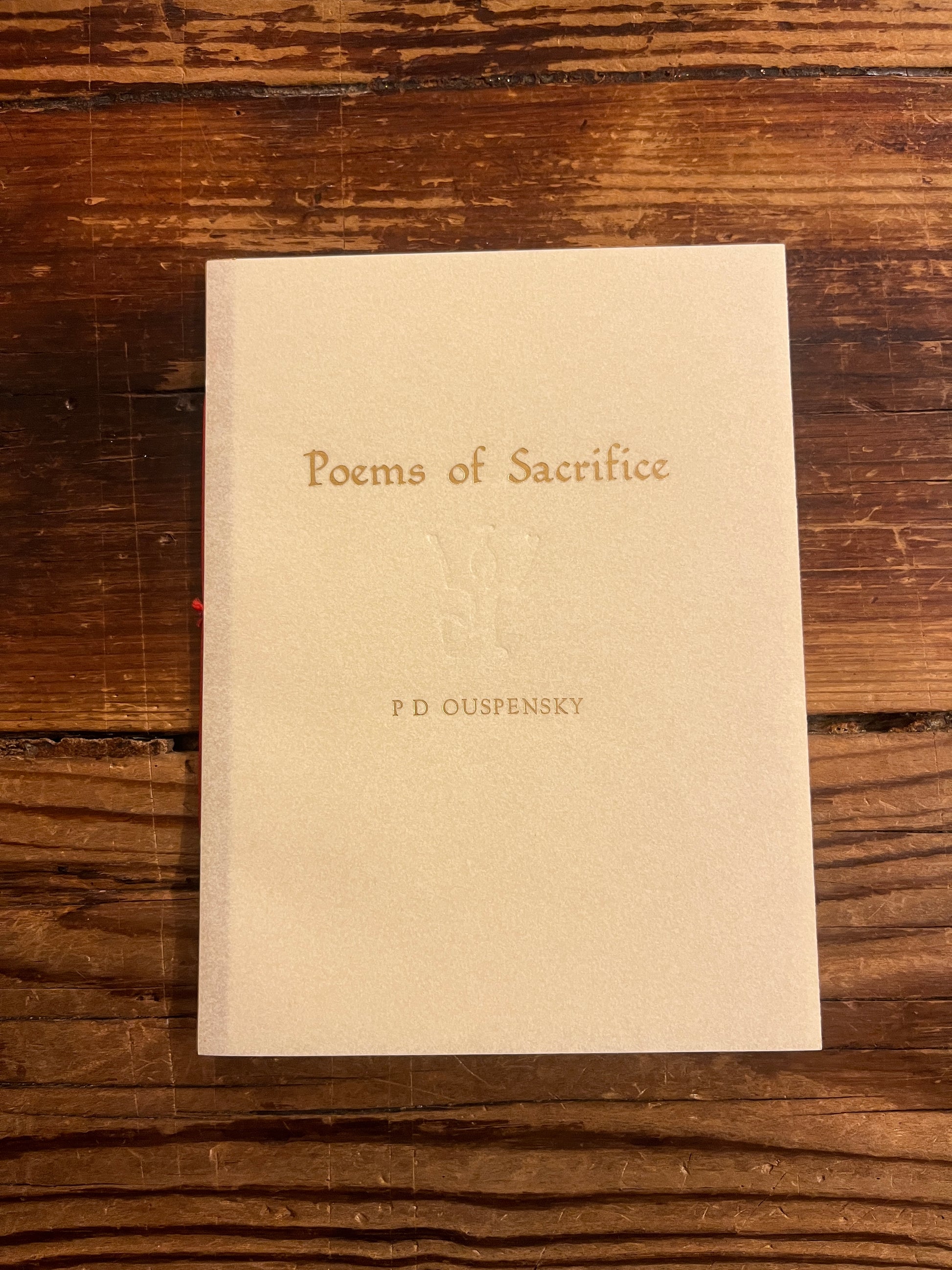 Beige book titled 'Poems of Sacrifice' by P.D. Ouspensky on a wooden surface