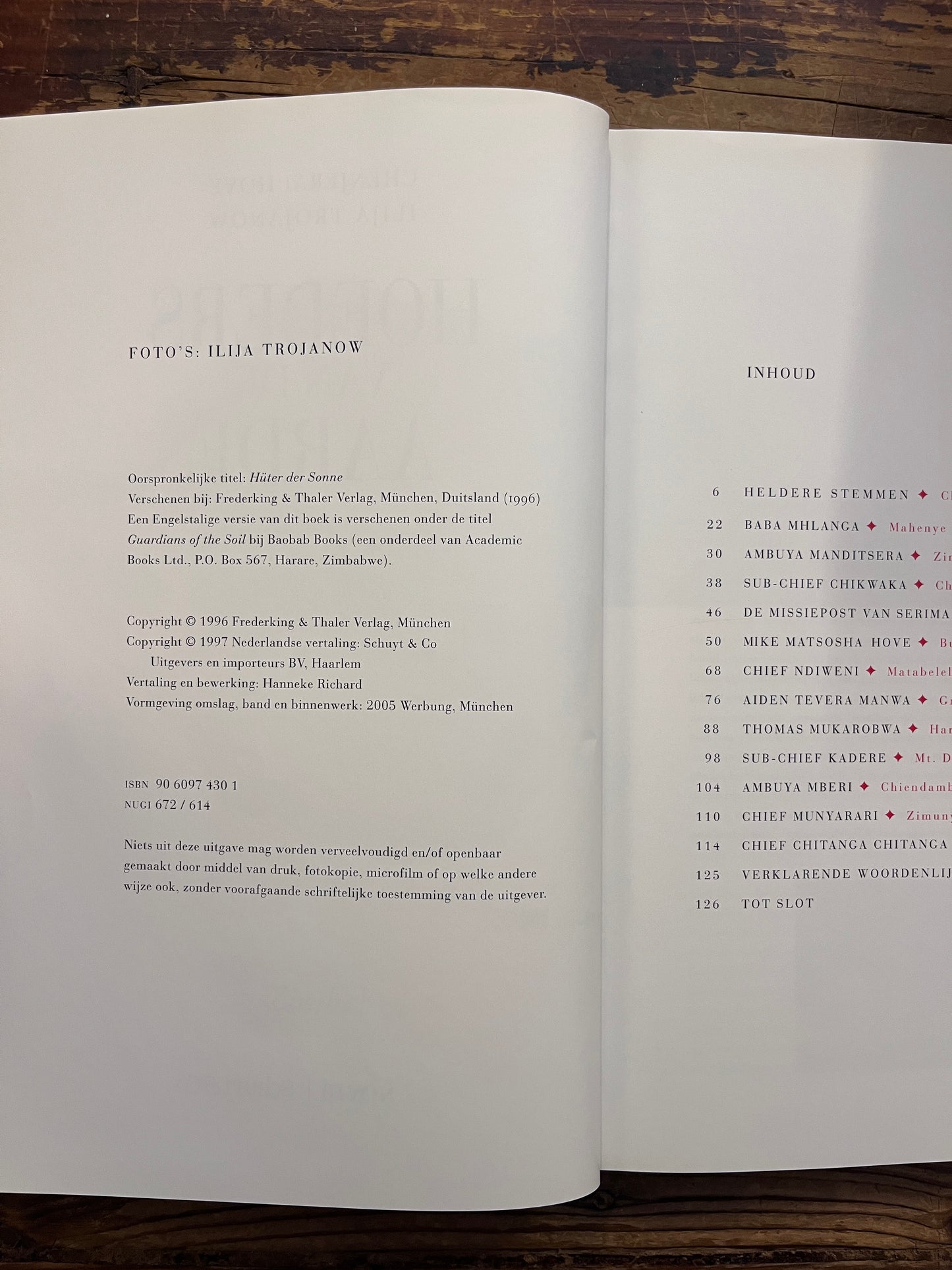 Open boek met de titel 'Hoeders van de Aarde' door Chenjerai Hove en Ilija Trojanow op een houten achtergrond 