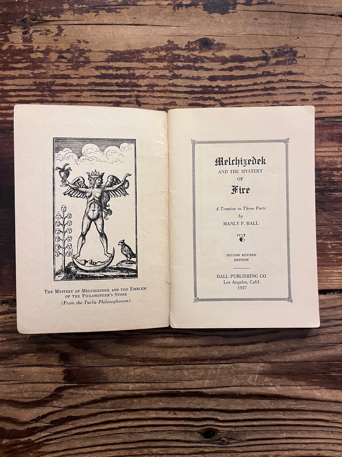 Open booklet titled 'Melchizedek and the mystery of fire' by Manly P. Hall on a wooden surface 