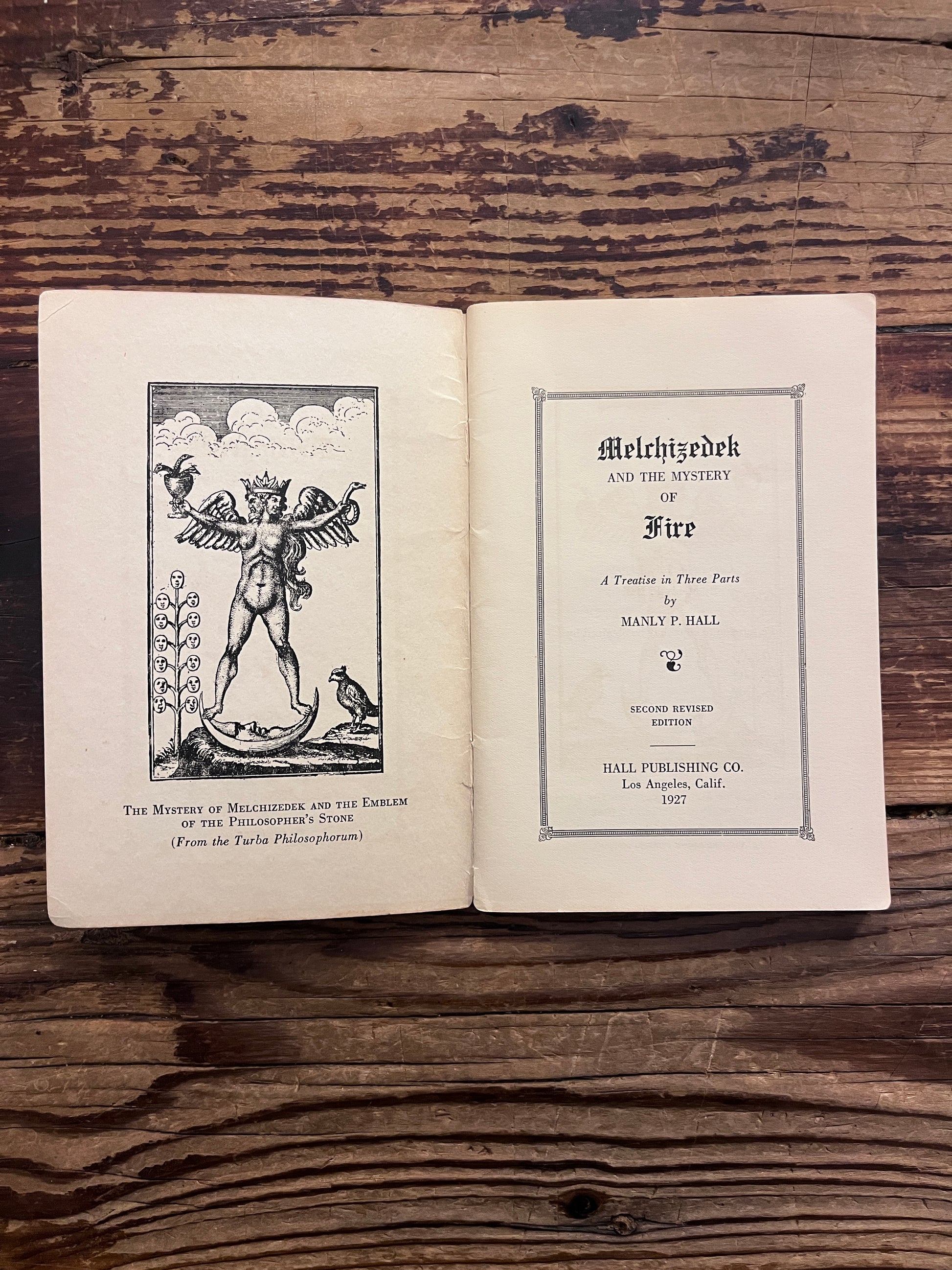 Open booklet titled 'Melchizedek and the mystery of fire' by Manly P. Hall on a wooden surface 