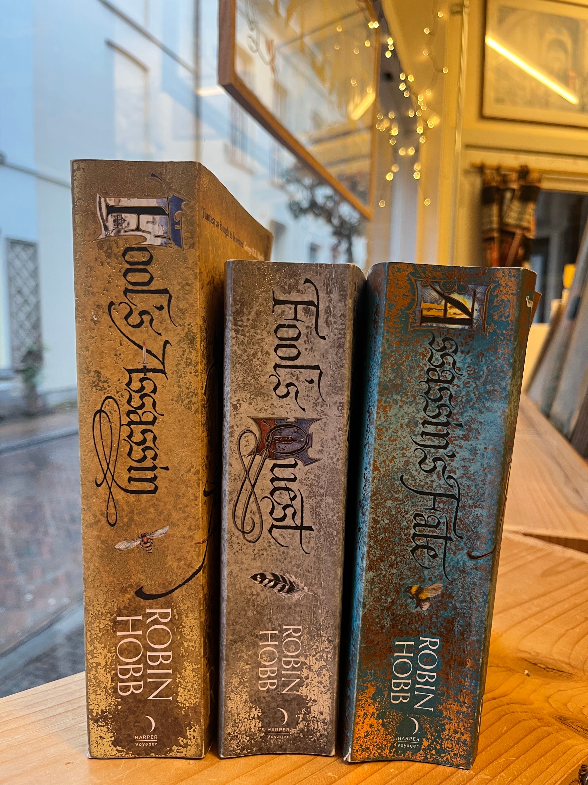 Three books titled 'Assassin's Fate', 'Fool's Quest', and 'Fool's Assassin' by Robin Hobb on a wooden surface.