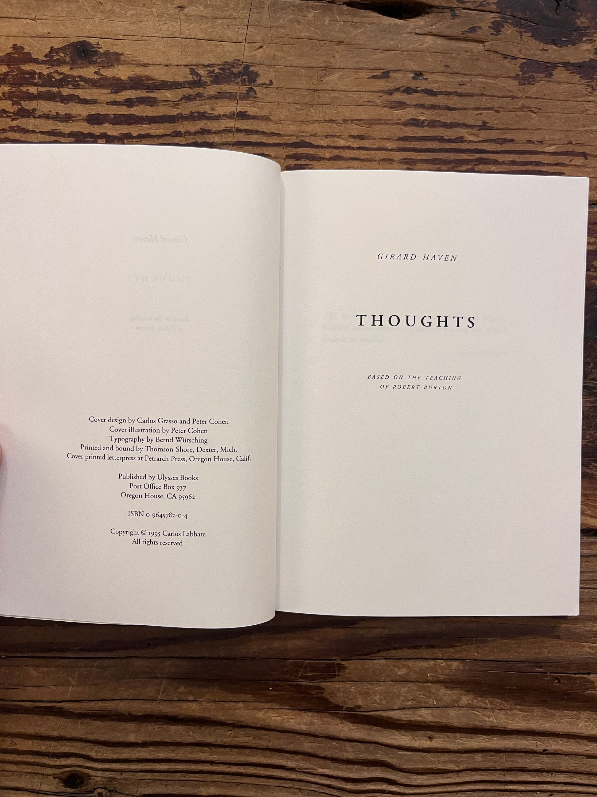 Open book titled 'thoughts based on the teachings of Robert Burton' by Girard Haven on a wooden surface 