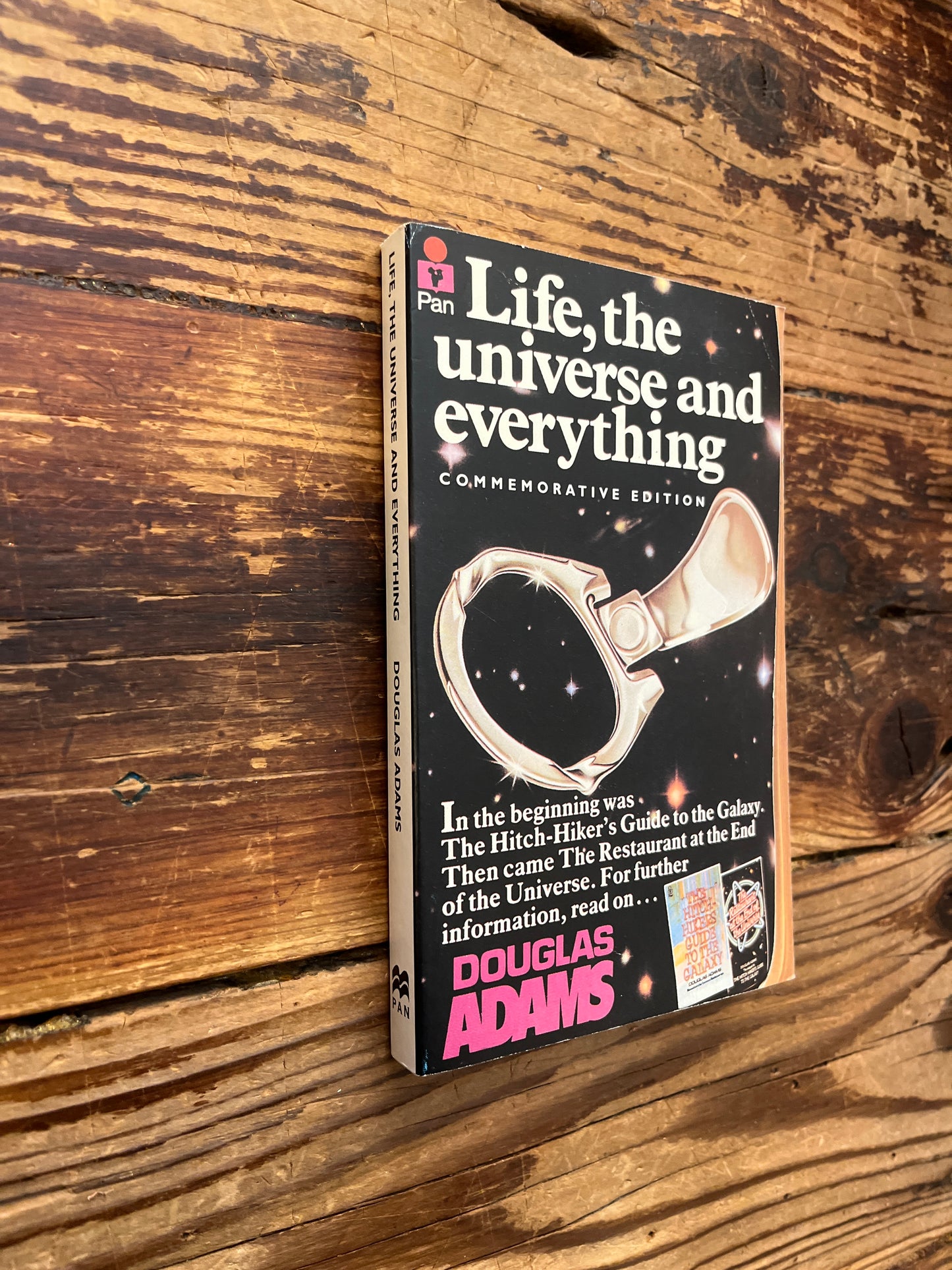 Book cover of 'Life, the Universe and Everything' by Douglas Adams on a wooden surface