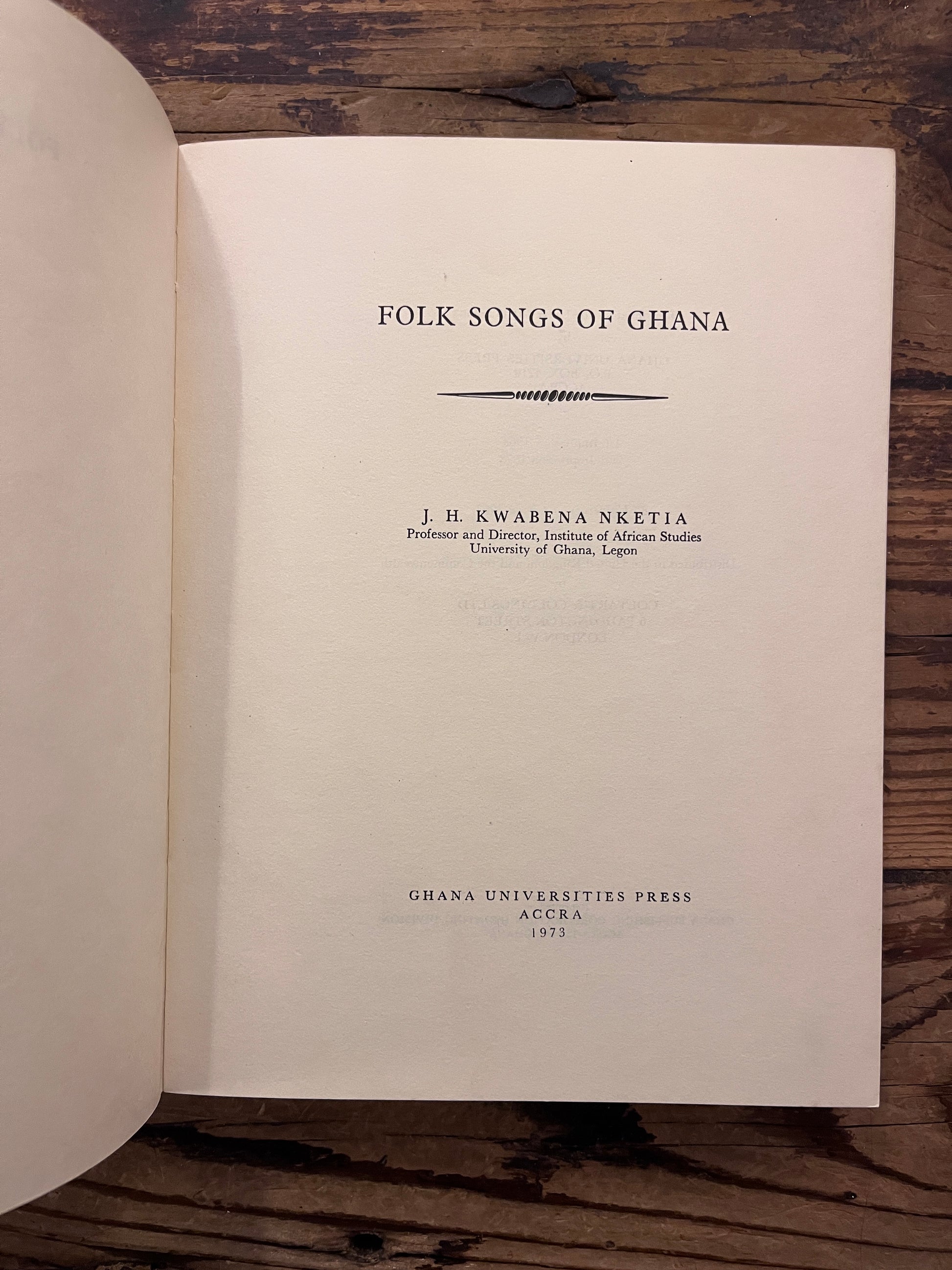 Title page of book titled 'Folk Songs of Ghana' by J.H. Kwabena Nketia on a wooden surface 