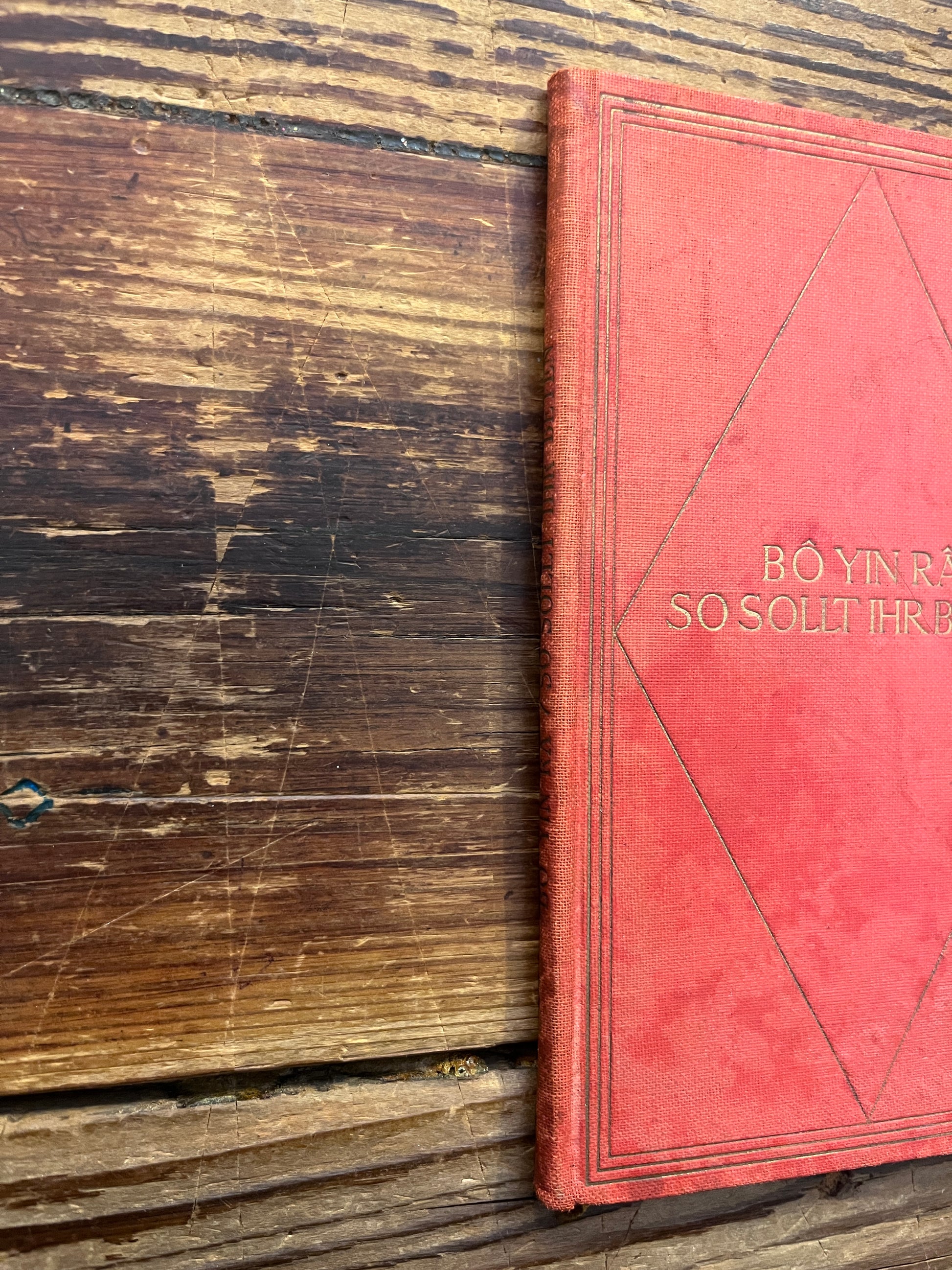 red cloth bound booklet with gold gilded letters with the title 'So Sollt Ihr Beten' by Bo Yin Ra on a wooden surface 
