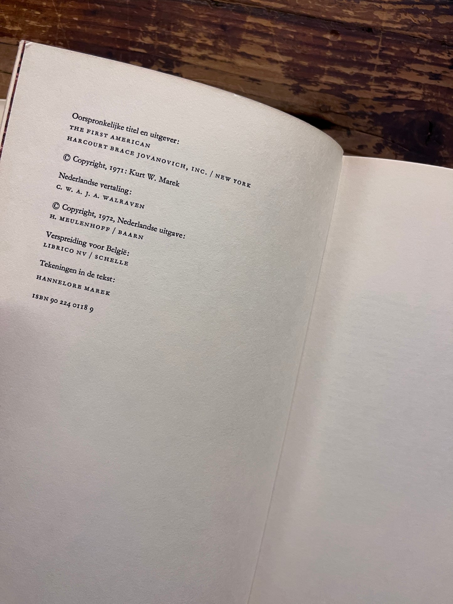 Uitgevers pagina van een hardcover boek met de titel 'De Eerste Amerikaan' by C.W. Ceram op een houten achtergrond 