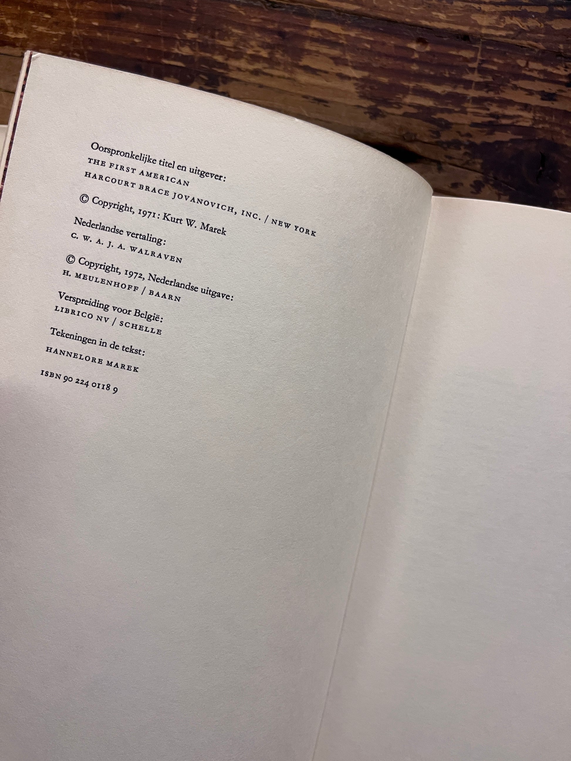 Uitgevers pagina van een hardcover boek met de titel 'De Eerste Amerikaan' by C.W. Ceram op een houten achtergrond 