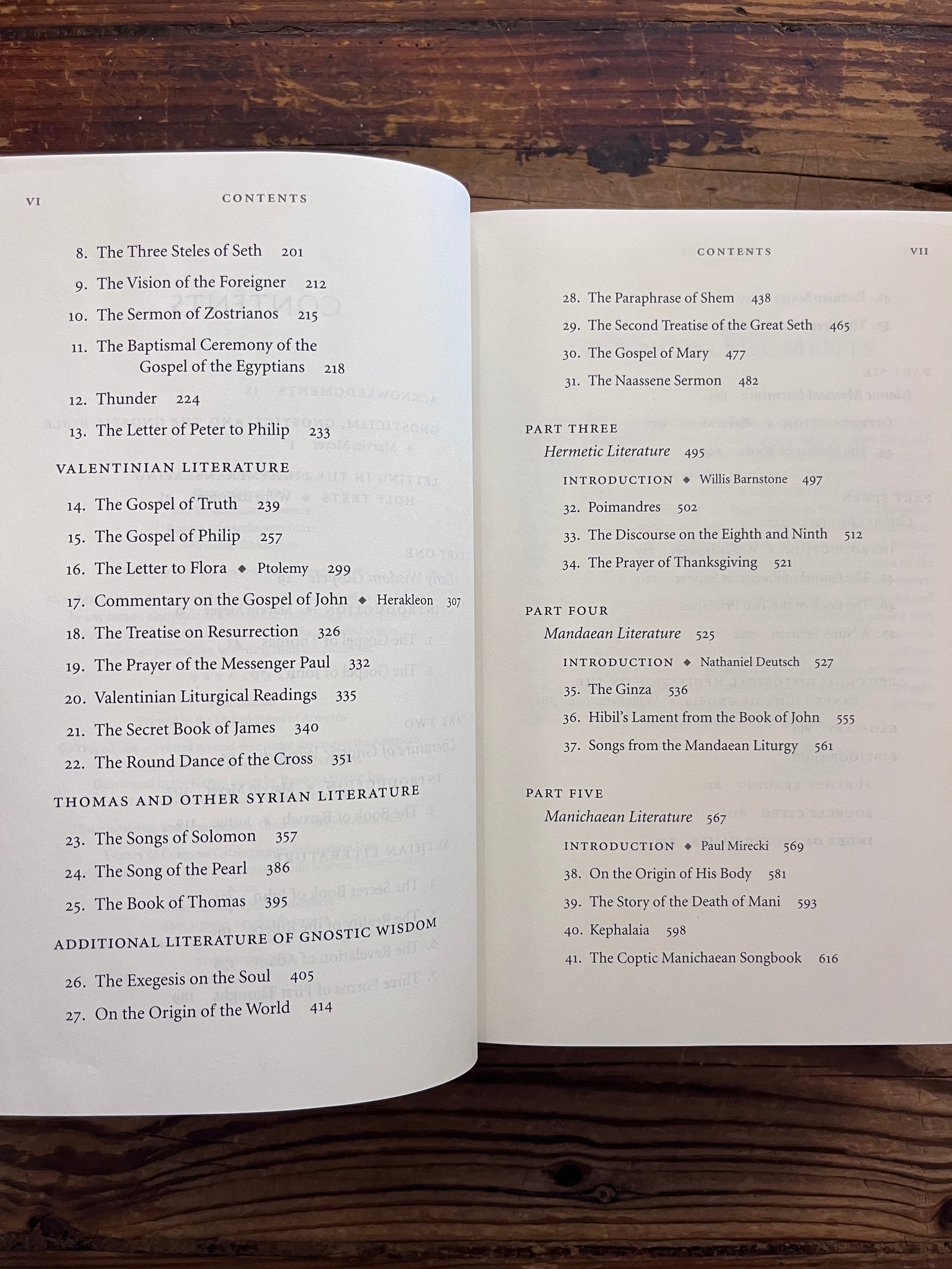 Open book titled 'he Gnostic Bible' edited by Willis Barnstone and Marvin Meyer, on a wooden surface