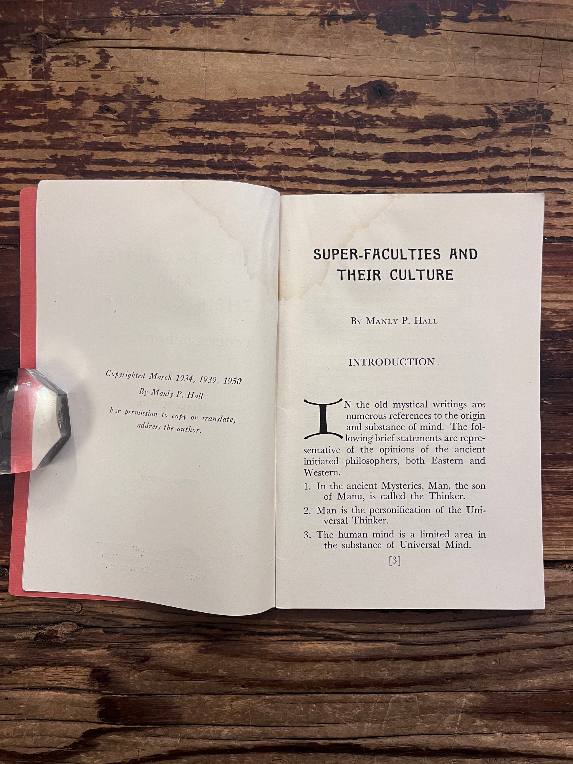 Open book titled 'Super Faculties and Their Culture' by Manly P. Hall on a wooden surface