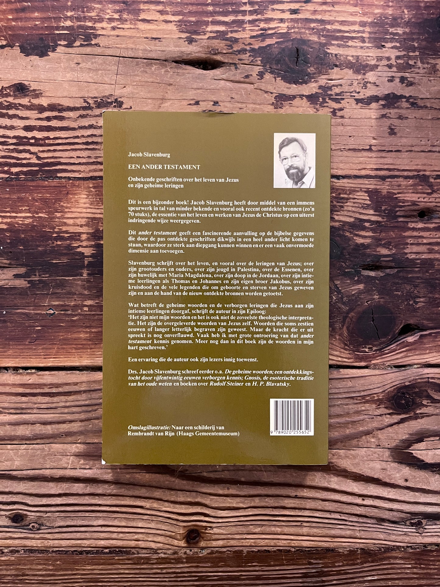 Achterkant van boek met de titel 'Een ander testament' door J. Slavenburg op een houten achtergrond 