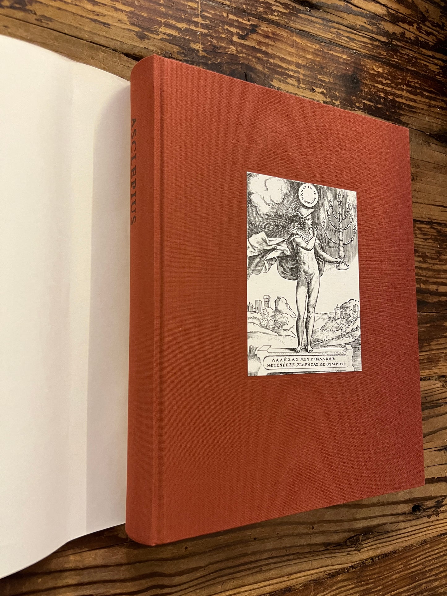 Voorkant zonder stof omslag van 'Asclepius' ingeleid, vertaald en toegelicht door G. Quispel op een houten achtergrond 