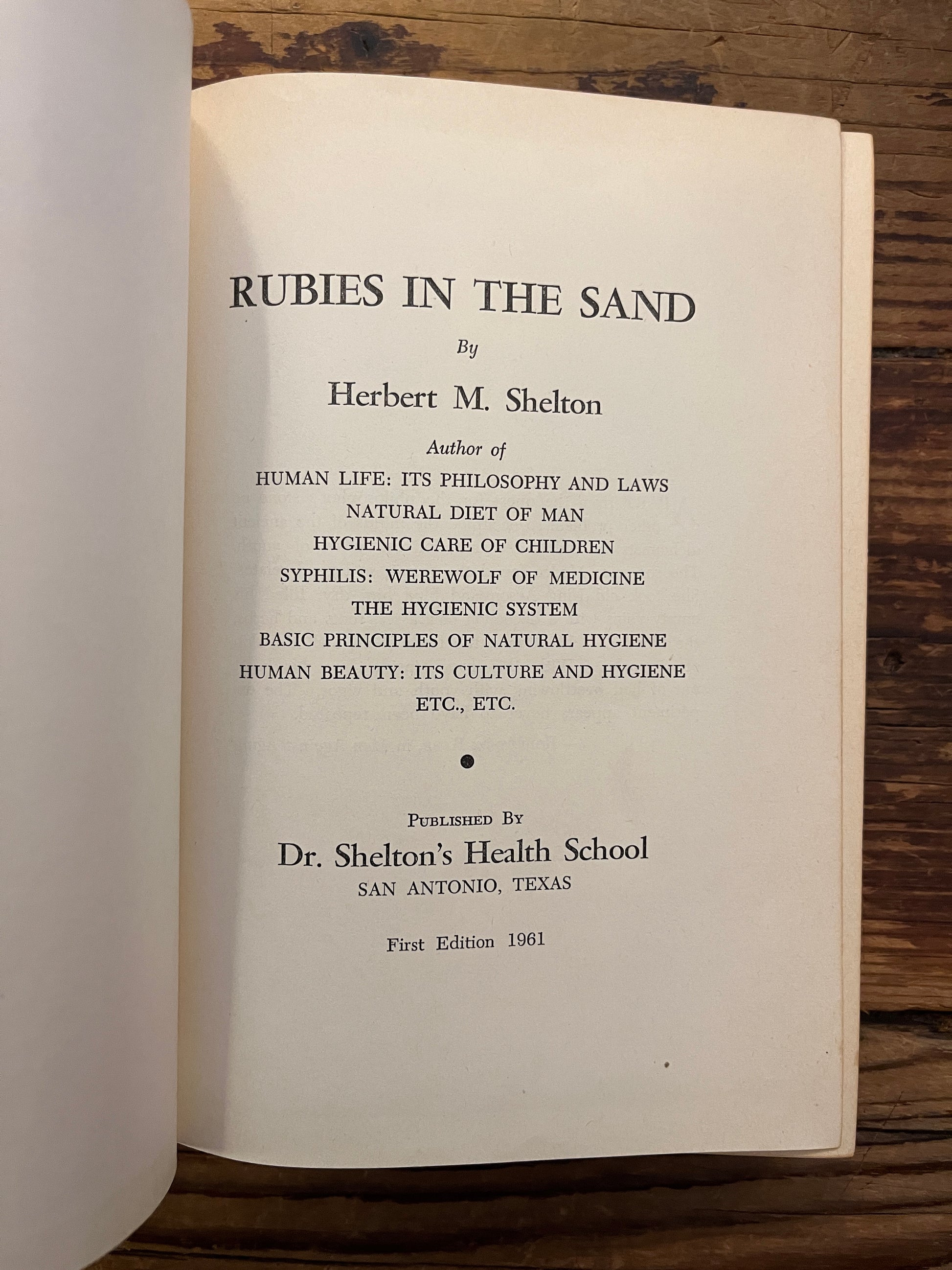 Open book titled 'Rubies in the Sand' by Herbert M. Shelton on a wooden surface