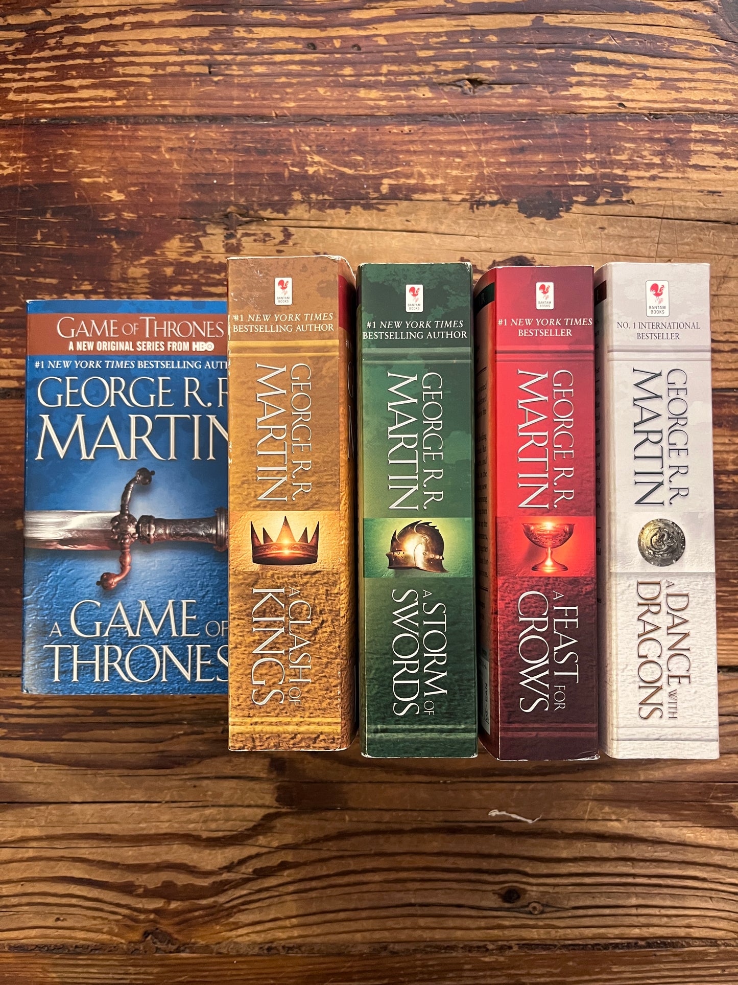 Spines of the five first books by George R. R. Martin on a wooden surface. in order 'A Game of thrones', 'A clash of kings', 'A storm of swords', 'A feast for crows' and 'A dance with dragons 