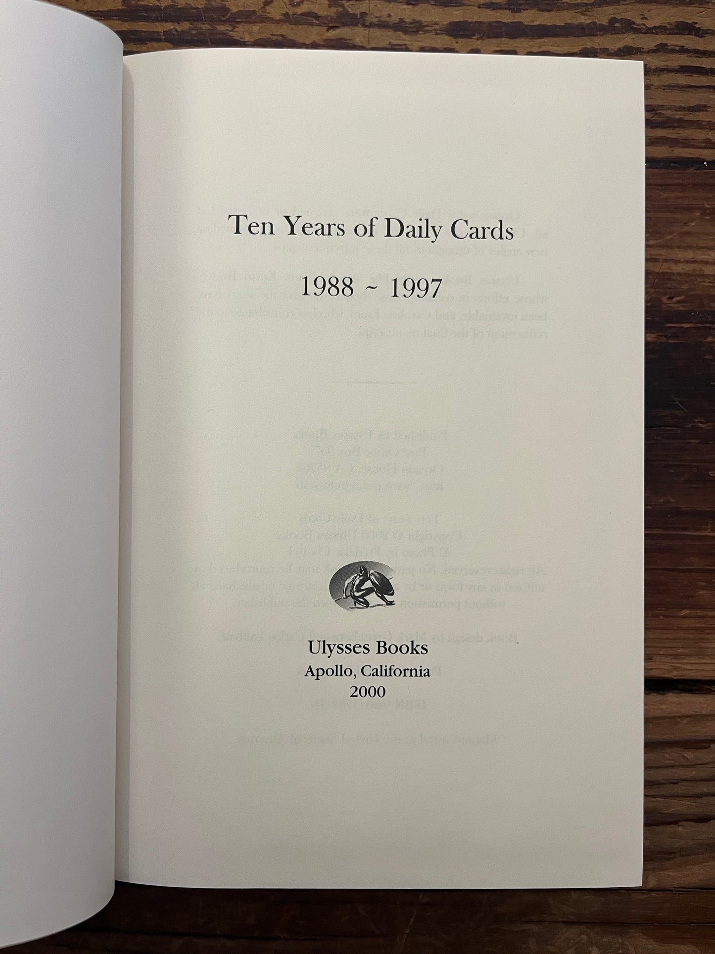 Open book with the title 'Ten Years of Daily Cards' by Robert Burton on a wooden surface