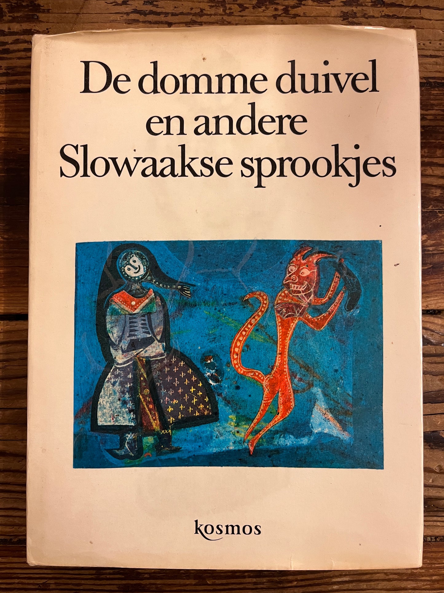 Voorkant met stof omslag van boek met de titel 'De domme duivel en andere Slowaakse sprookjes' op een houten tafel