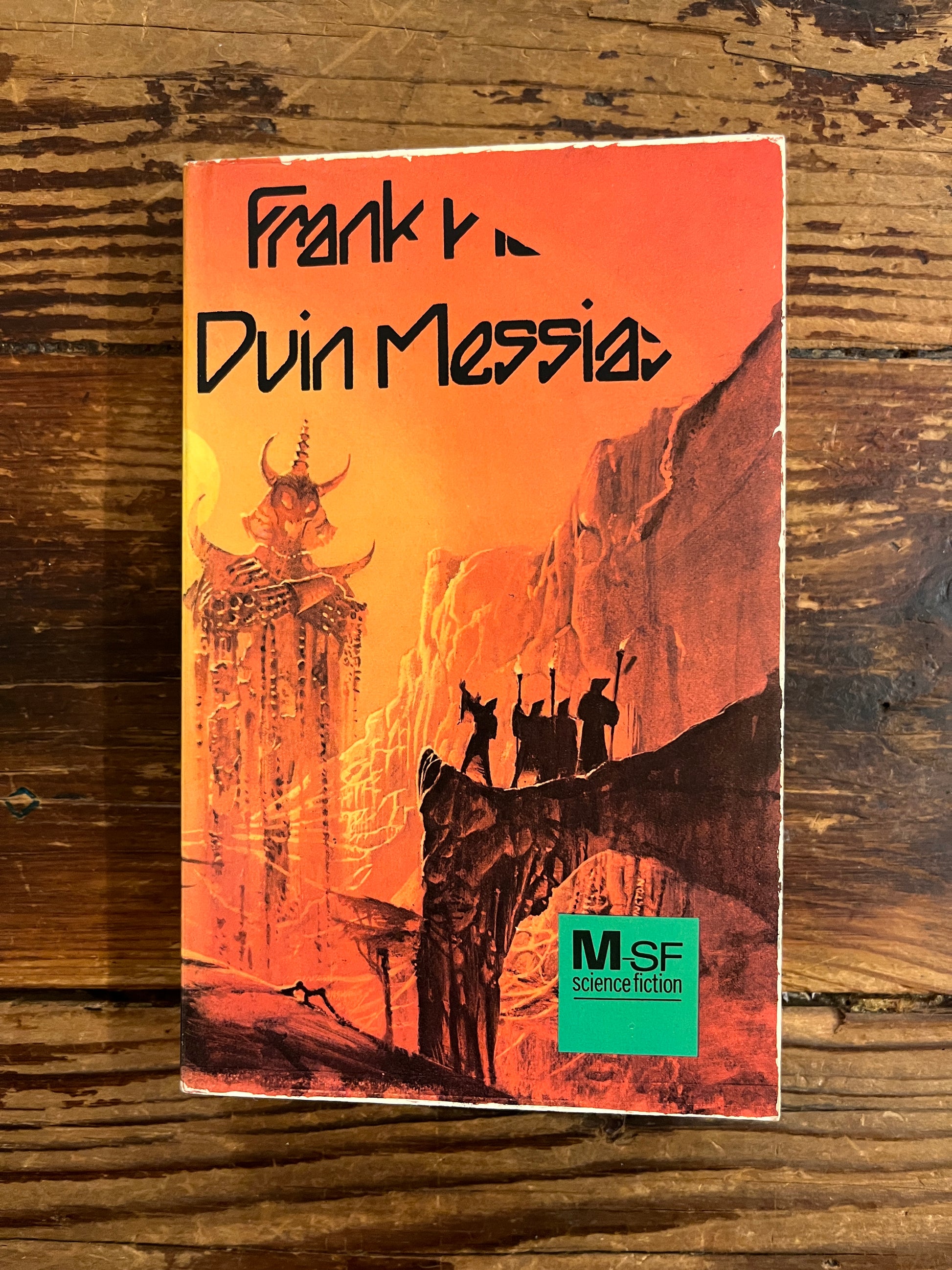 Voorkant van boek met de titel 'Duin Messias' door Frank Herbert op een houten achtergrond 