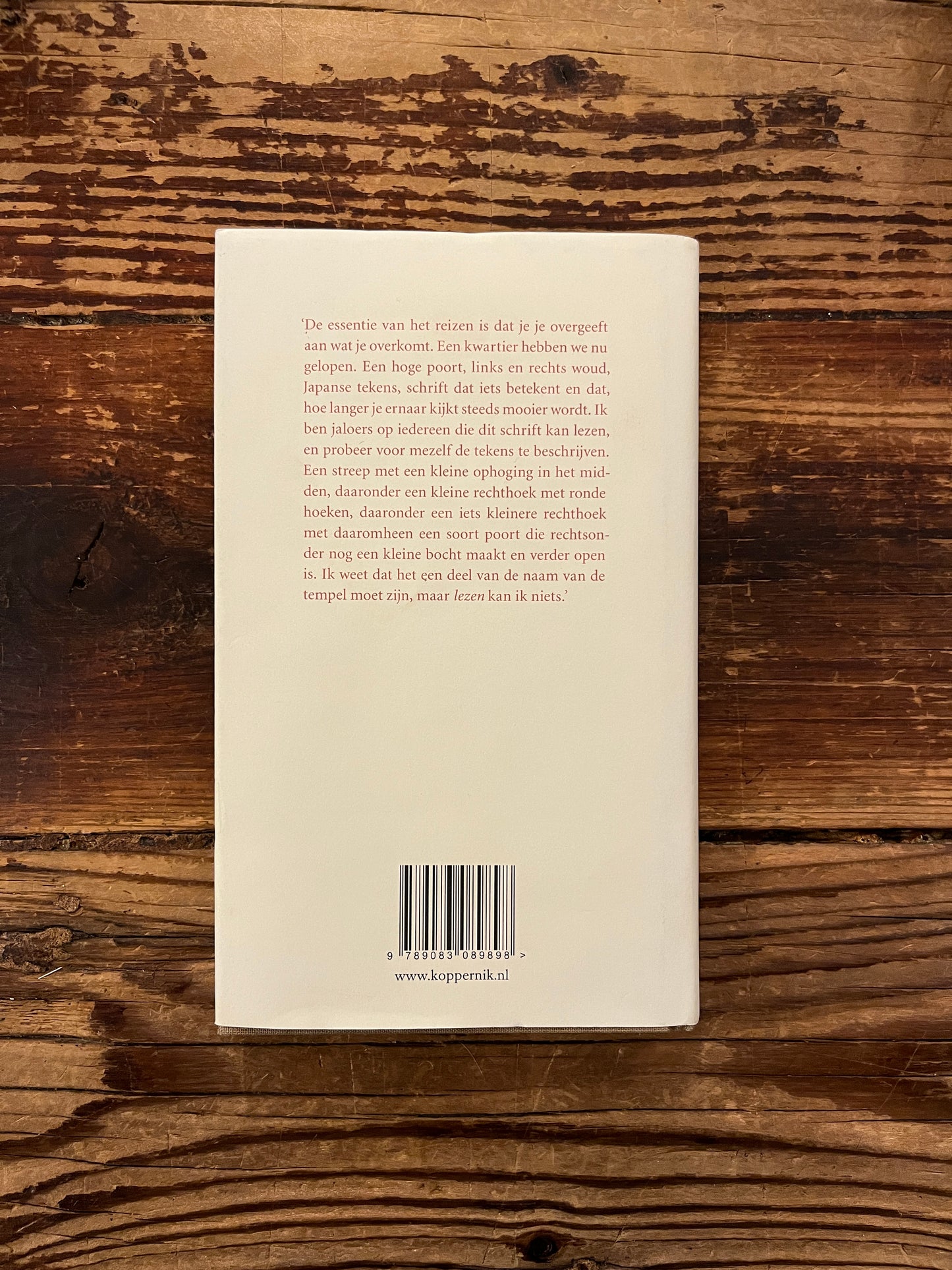 Achterkant  van boek met de titel 'Over het Japanse klooster Kozan-ji en de beroemde dierentekeningen' door Cees Nooteboom, op een houten achtergrond