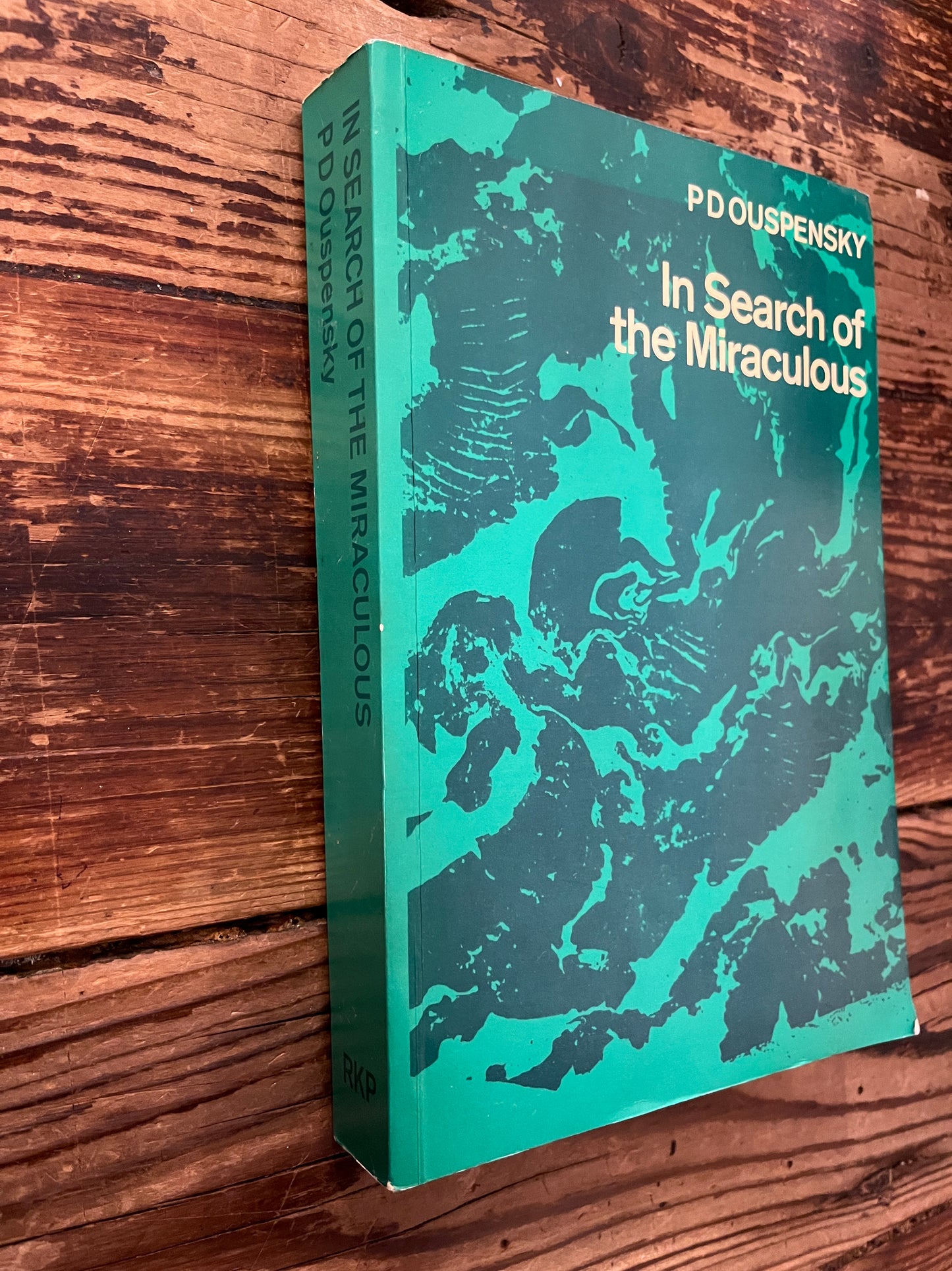 Cover and spine of book titled 'In Search of the Miraculous' by P.D. Ouspensky on a wooden surface