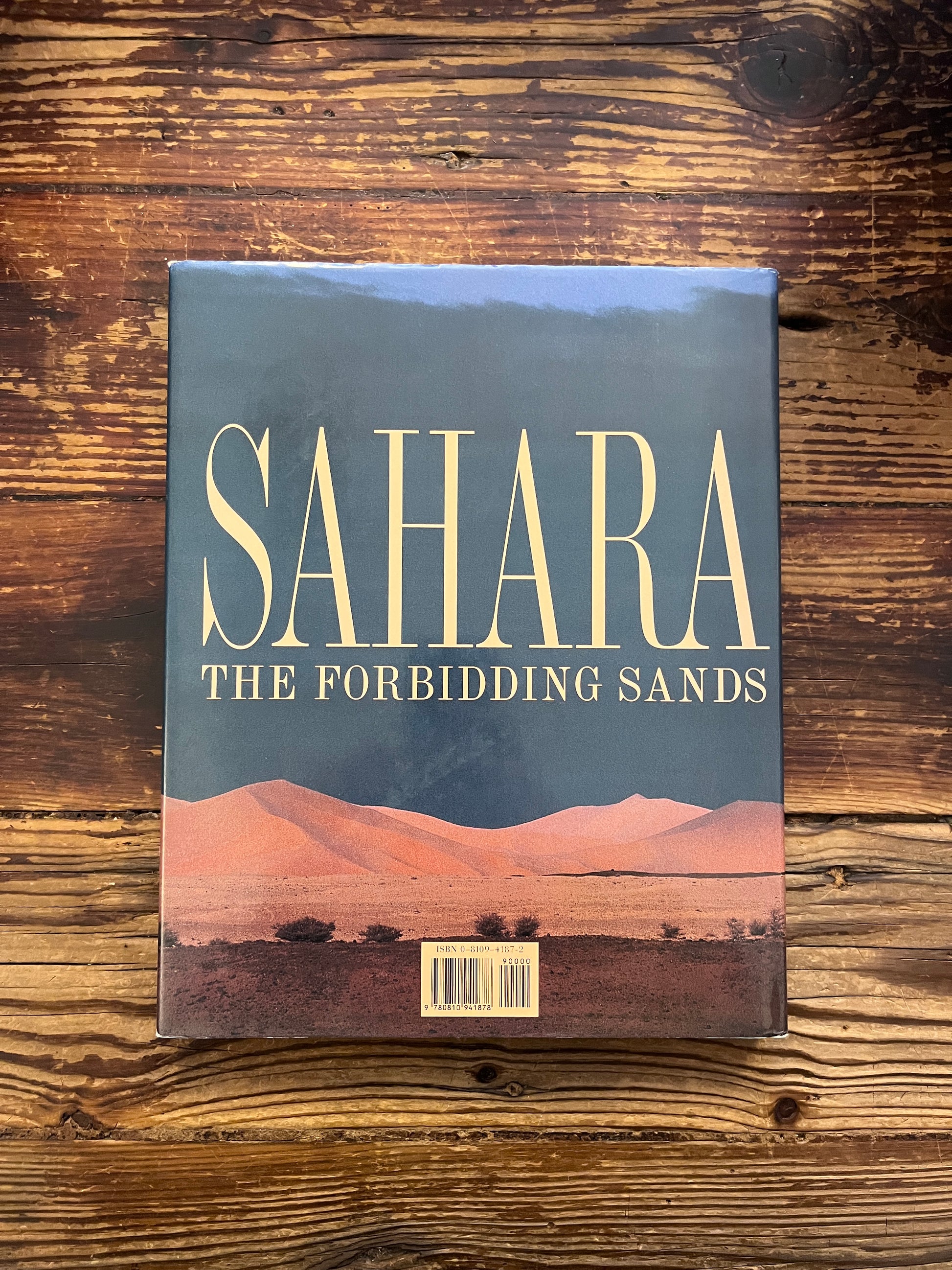 Back cover of book titled 'Sahara: The Forbidding Sands' by Jean-Marc Durou on a wooden surface