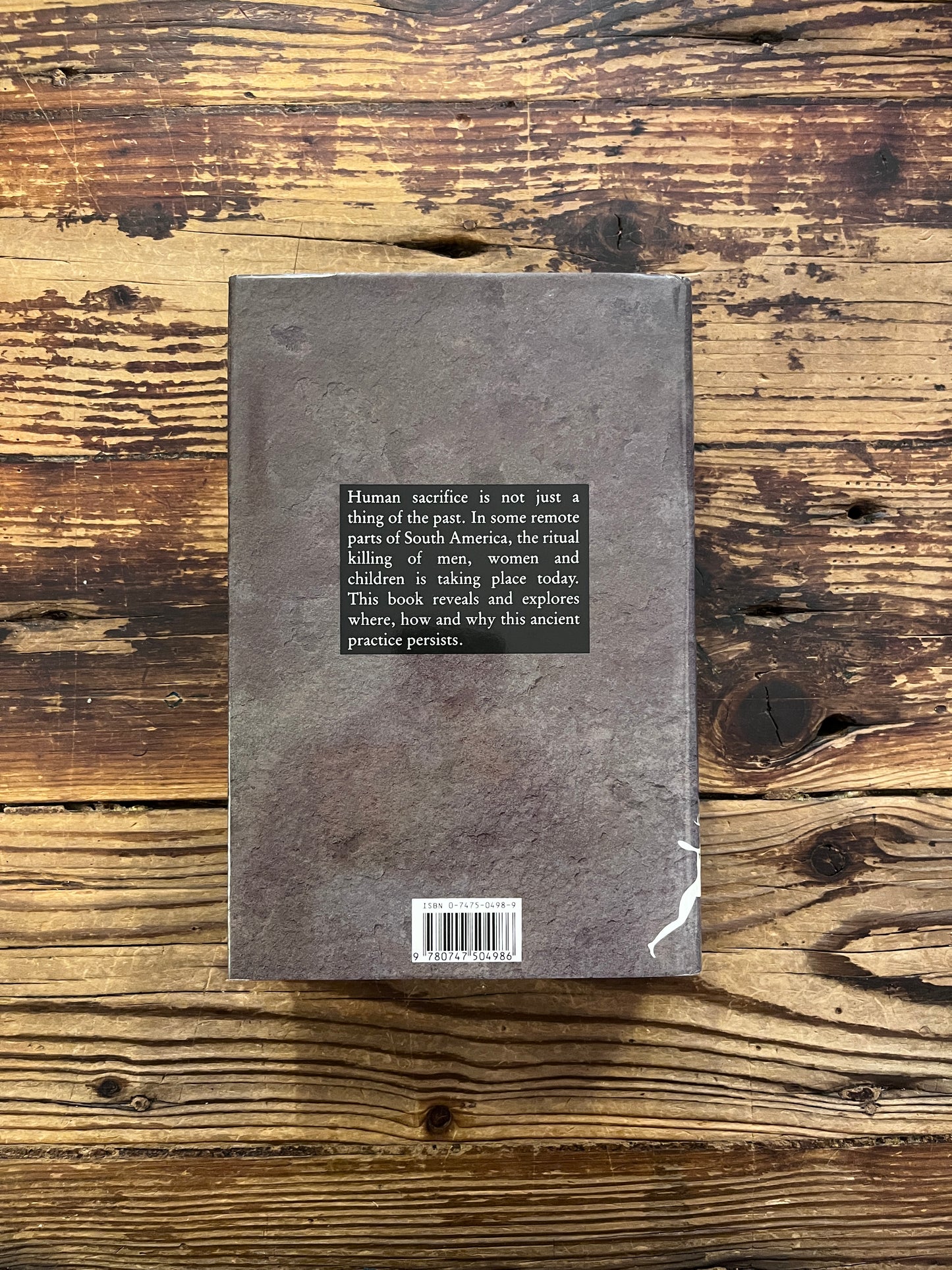 Back cover of a book with the title 'The Highest Altar: The Story of Human Sacrifice' by Patrick Tierney is displayed on a wooden surface