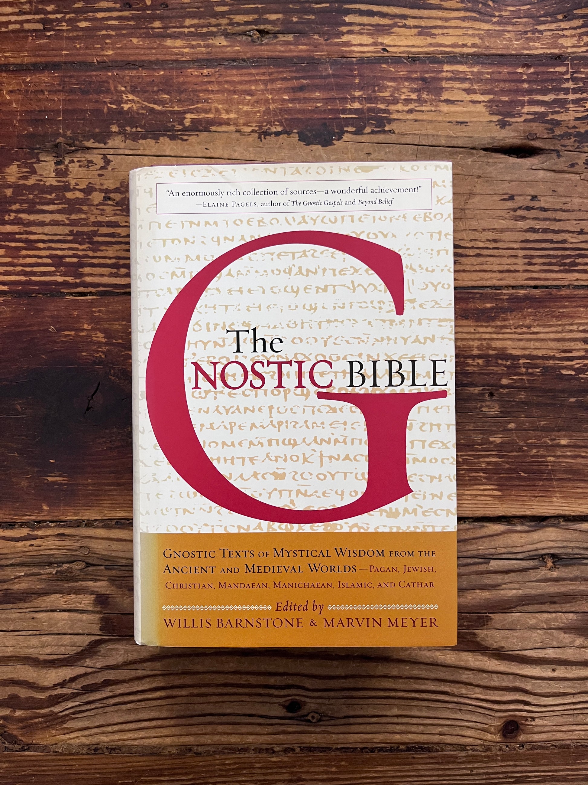 Front cover of book titled 'he Gnostic Bible' edited by Willis Barnstone and Marvin Meyer, on a wooden surface