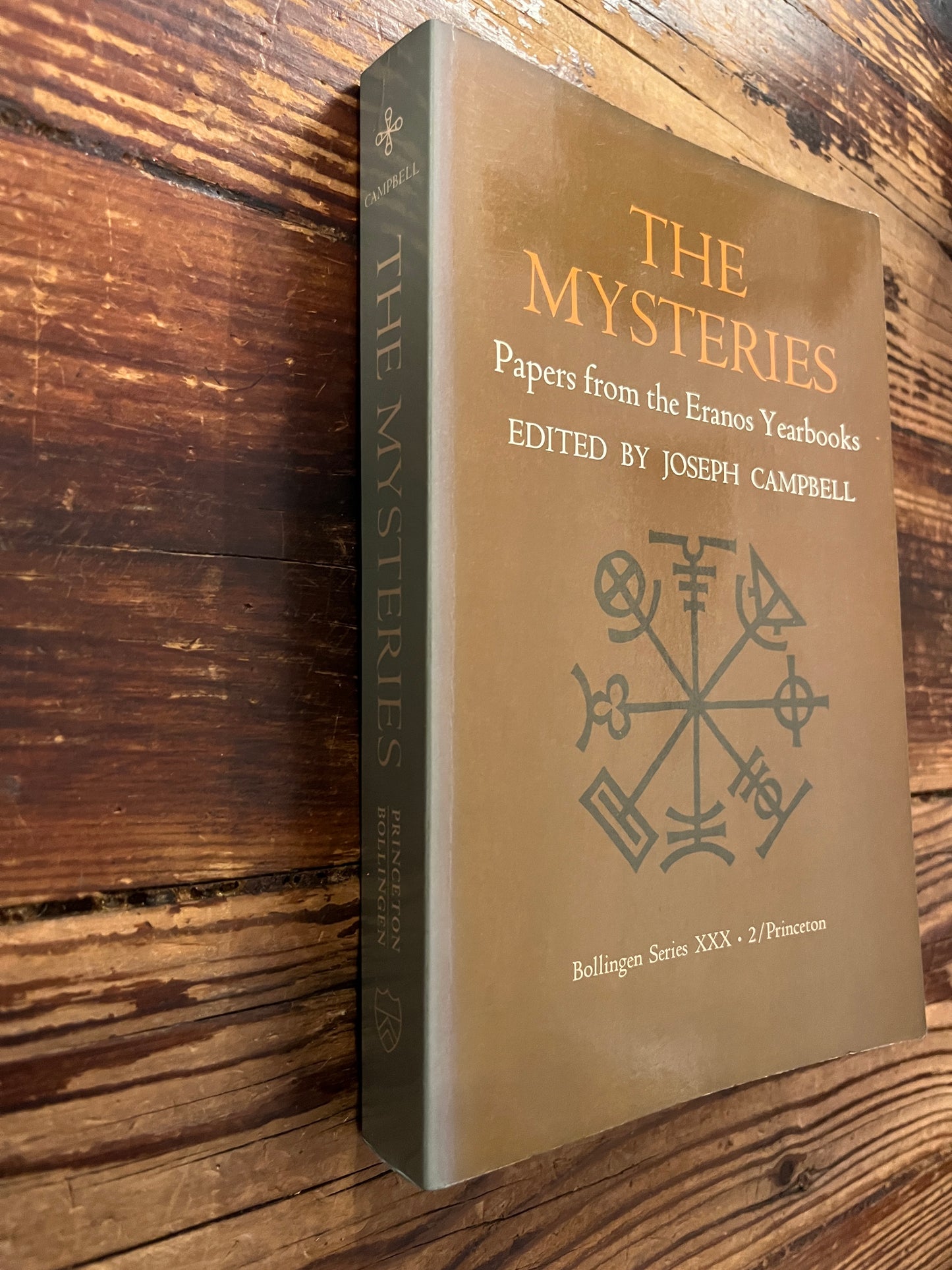 Book titled 'The Mysteries, papers from the Eranos Yearbooks' on a wooden surface