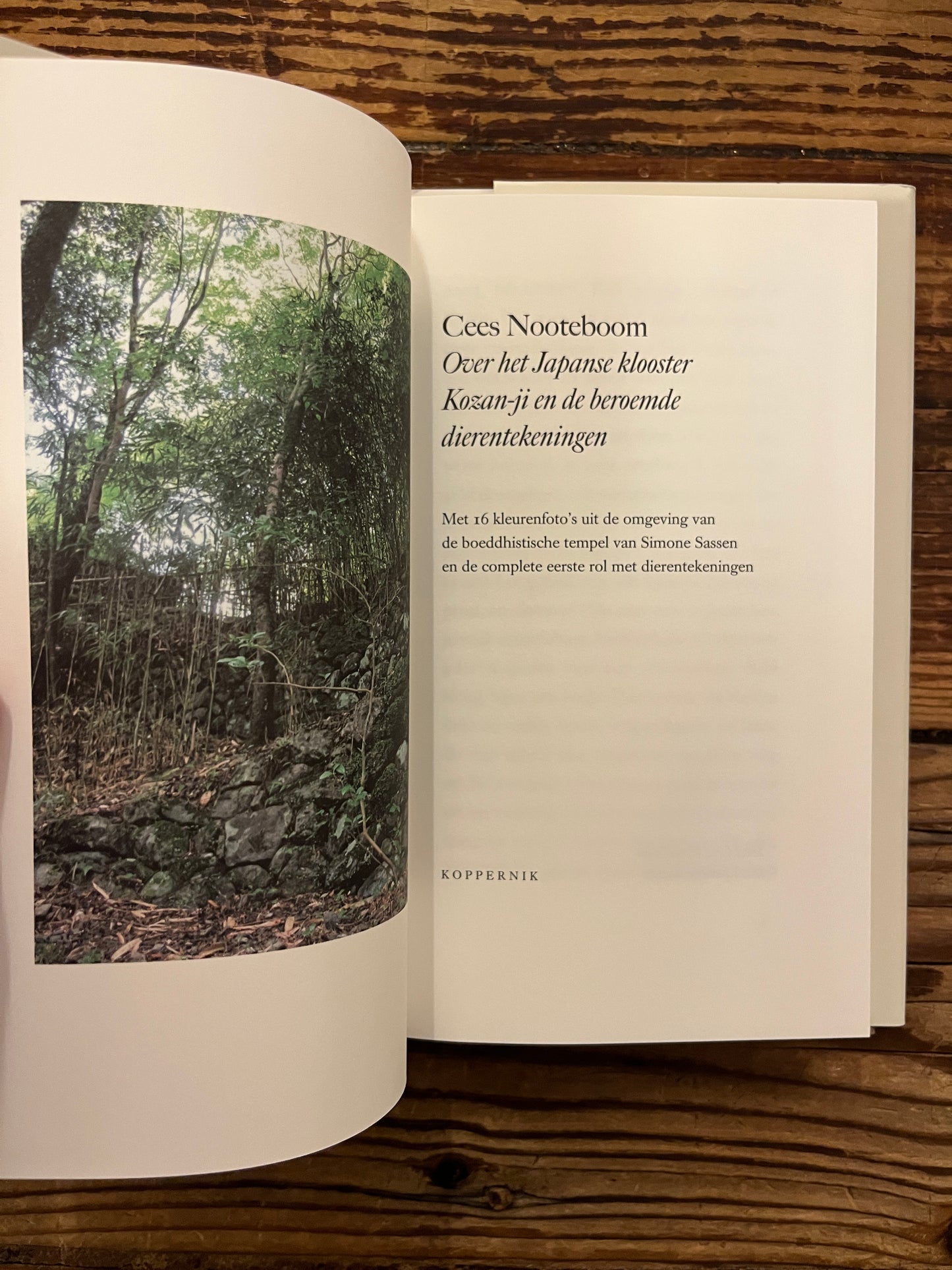 Open boek met de titel 'Over het Japanse klooster Kozan-ji en de beroemde dierentekeningen' door Cees Nooteboom, op een houten achtergrond
