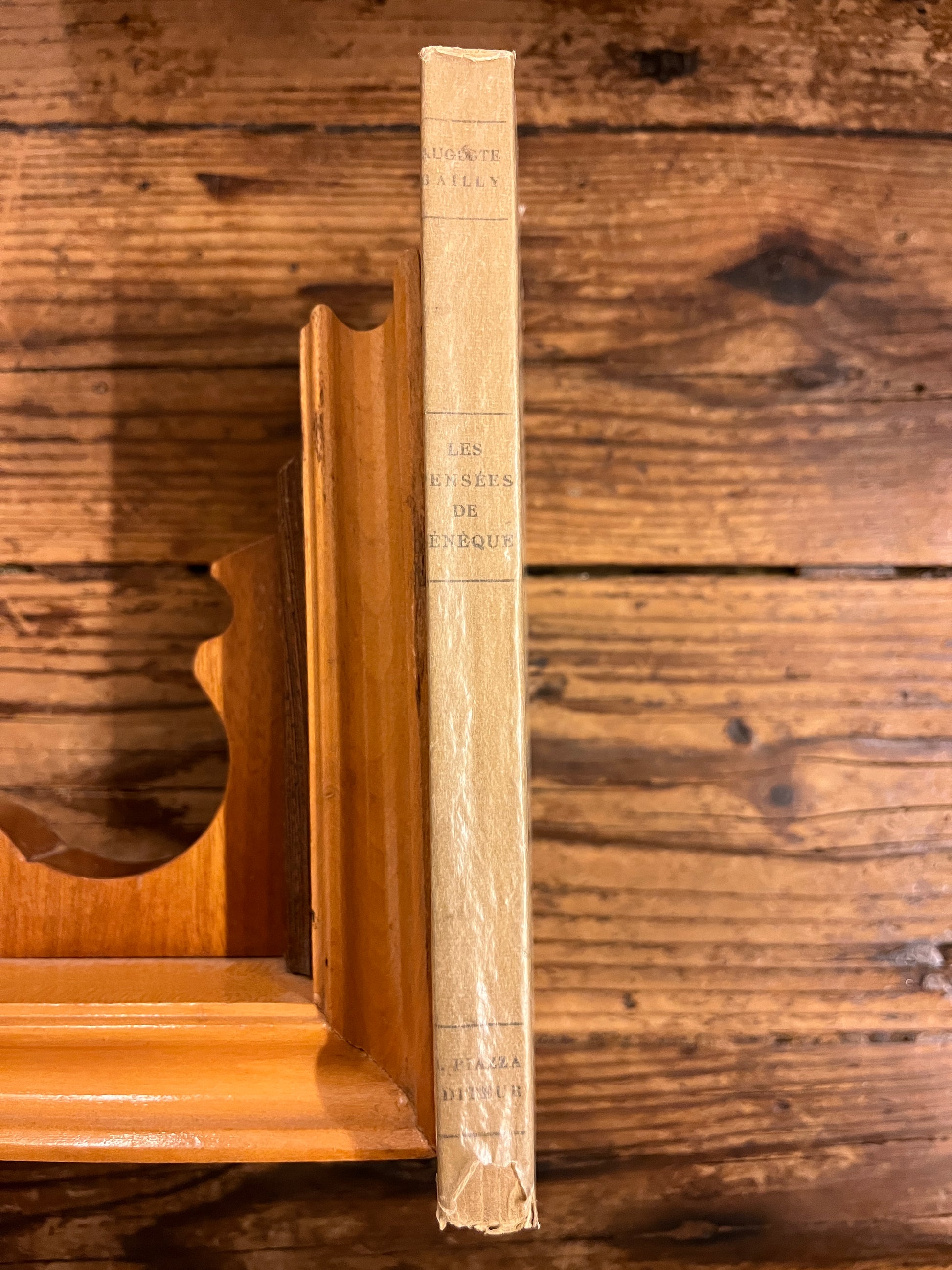 dos du livre "Les pensées de sénèque" sur fond de bois et soutenu par un calle livre en bois