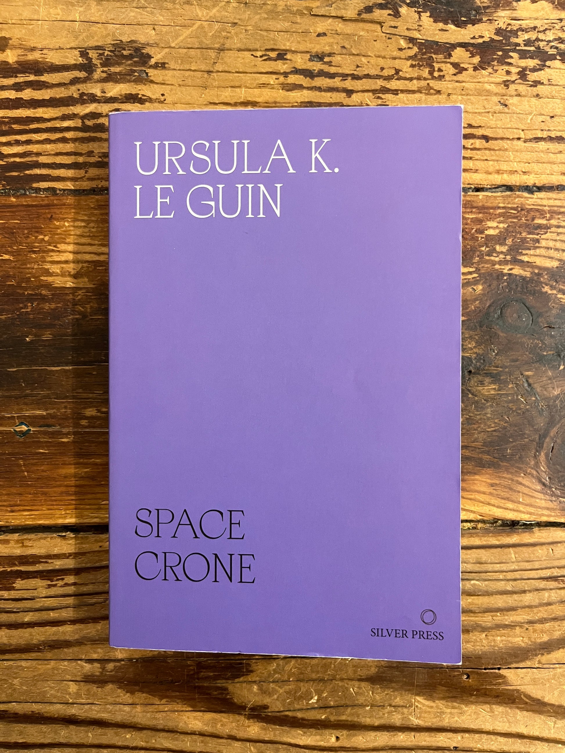 Front cover of purple book titled 'Space Crone' by Ursula K. Le Guin on a wooden surface